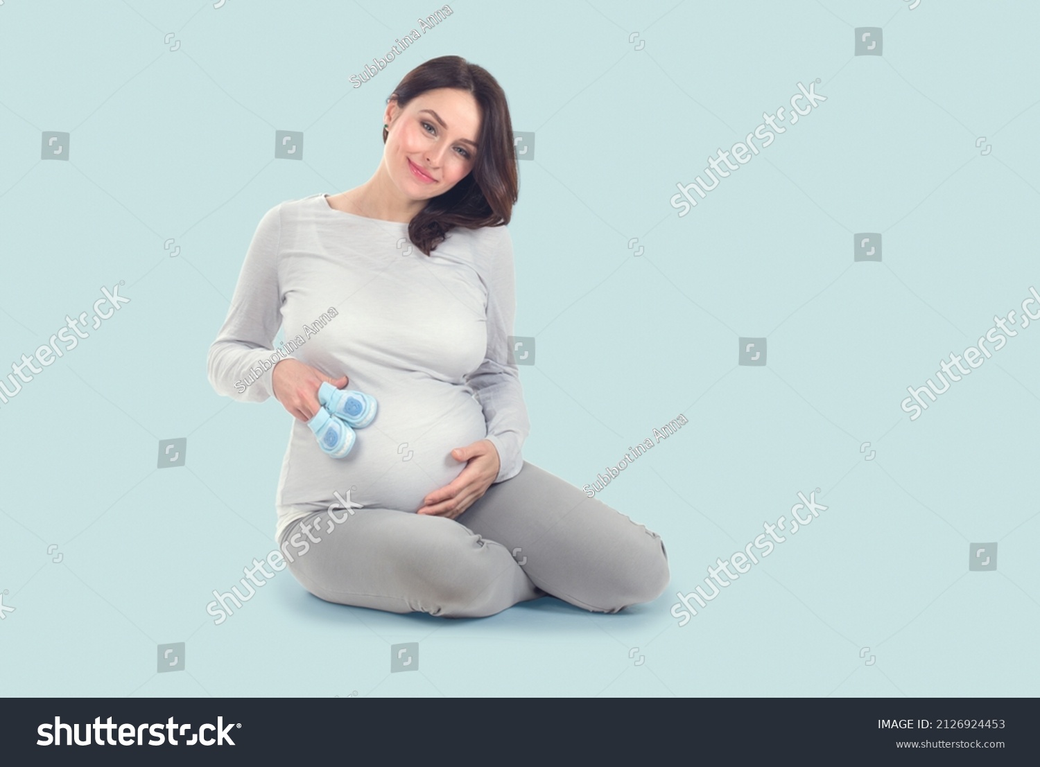 Pregnant Woman touching her belly. Pregnant middle aged mother's hands caressing her tummy. Healthy Pregnancy concept, Sitting Gravid female on blue background, full length portrait #2126924453