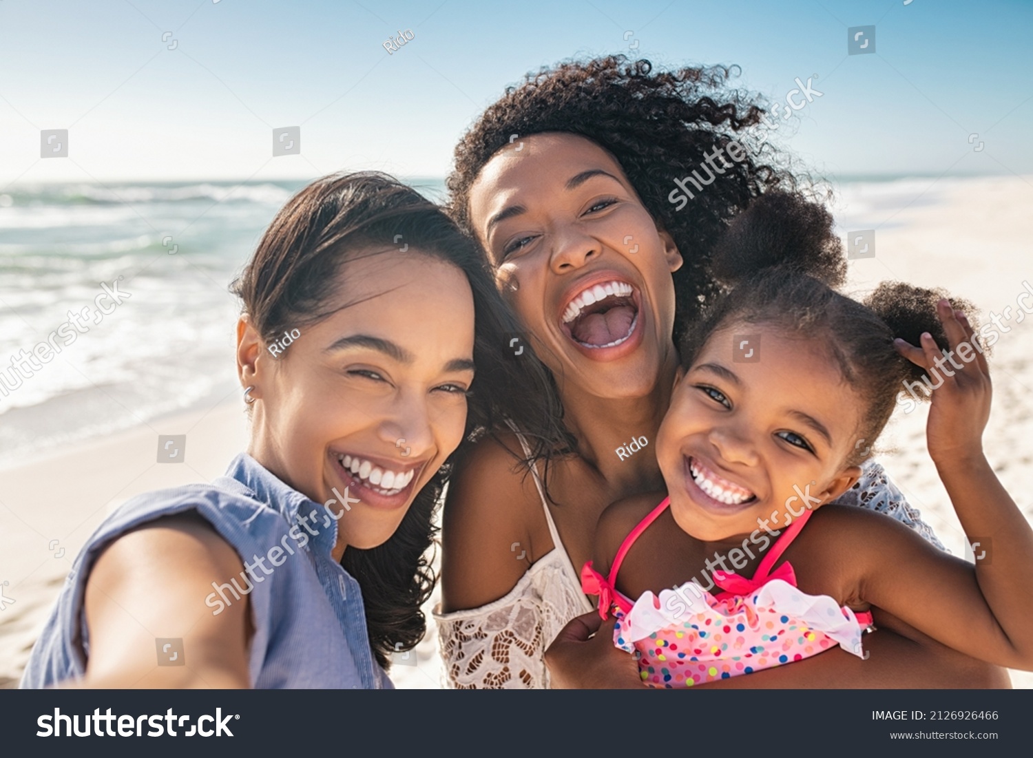 Portrait of smiling young african american woman with child taking selfie at beach with her best friend. Cheerful multiethnic gay couple enjoying at beach with daughter during summer holiday.  #2126926466