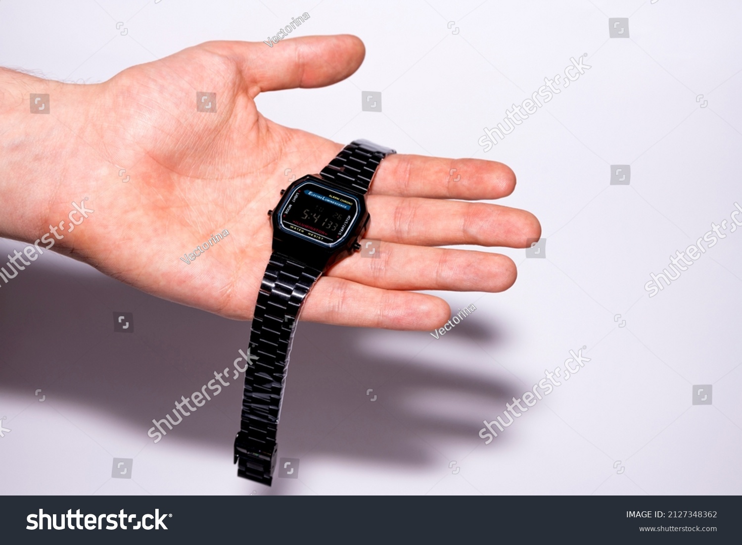 Black electronic watch in a metal case on a human palm. Brand new watch with protective film. Clock isolated on white background. #2127348362