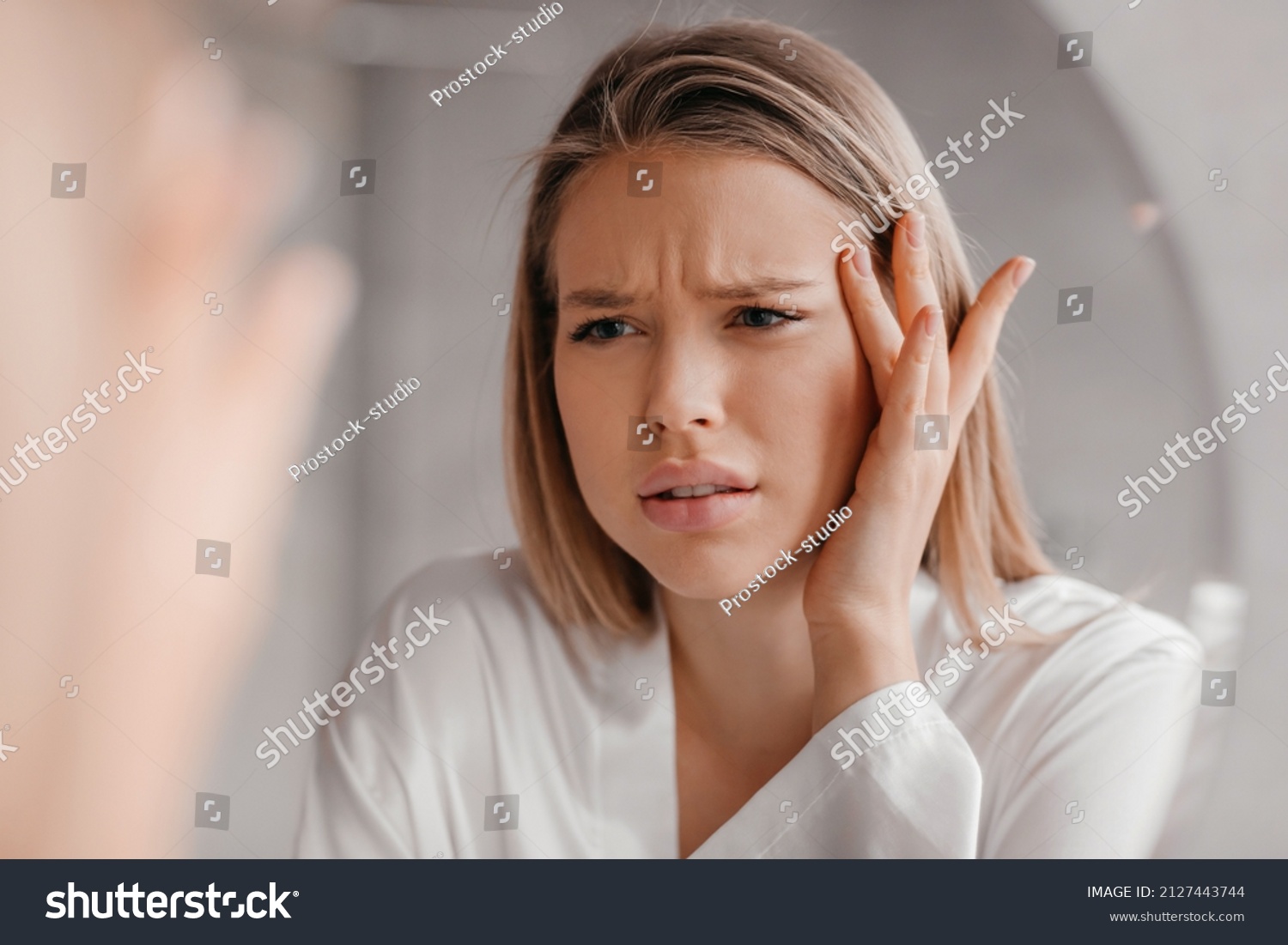 Mirror reflection of upset young lady looking at mirror and touching her forehead, having oily or dry skin problem, first wrinkles concept, bathroom interior #2127443744