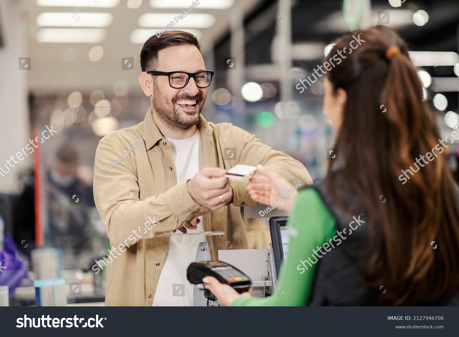 A smiling man giving credit card to a cashier and paying for groceries in supermarket. #2127946706