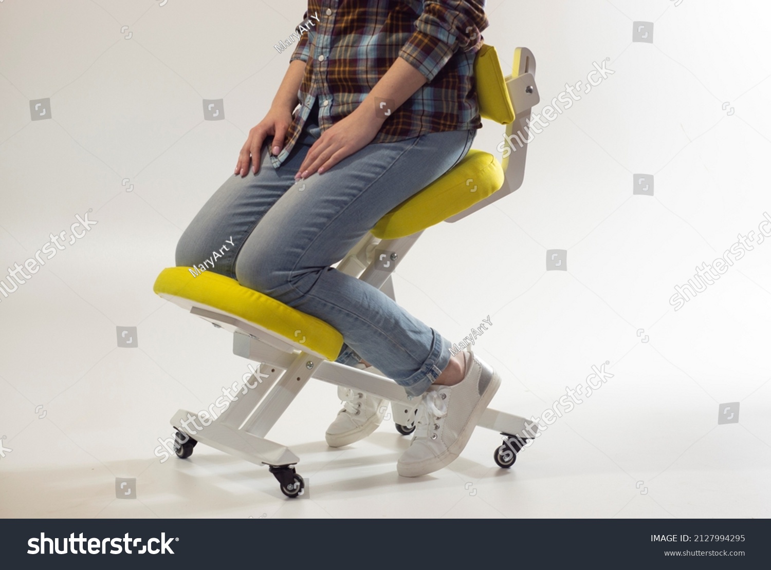 Woman is sitting on kneeling chair in office isolated on white. Ergonomic chair with wheels. Therapeutic stool with back support. Orthopaedic stool for desk based distance work from home. #2127994295