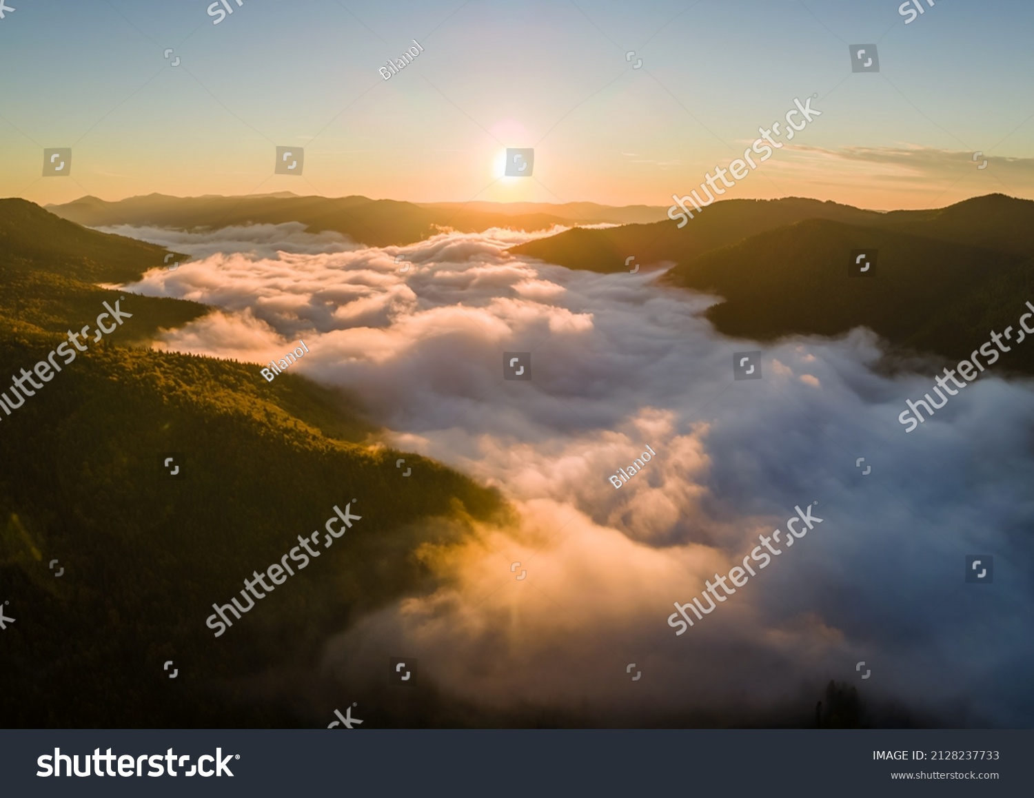 Aerial view of foggy evening over dark pine forest trees at bright sunset. Amazingl scenery of wild mountain woodland at dusk #2128237733