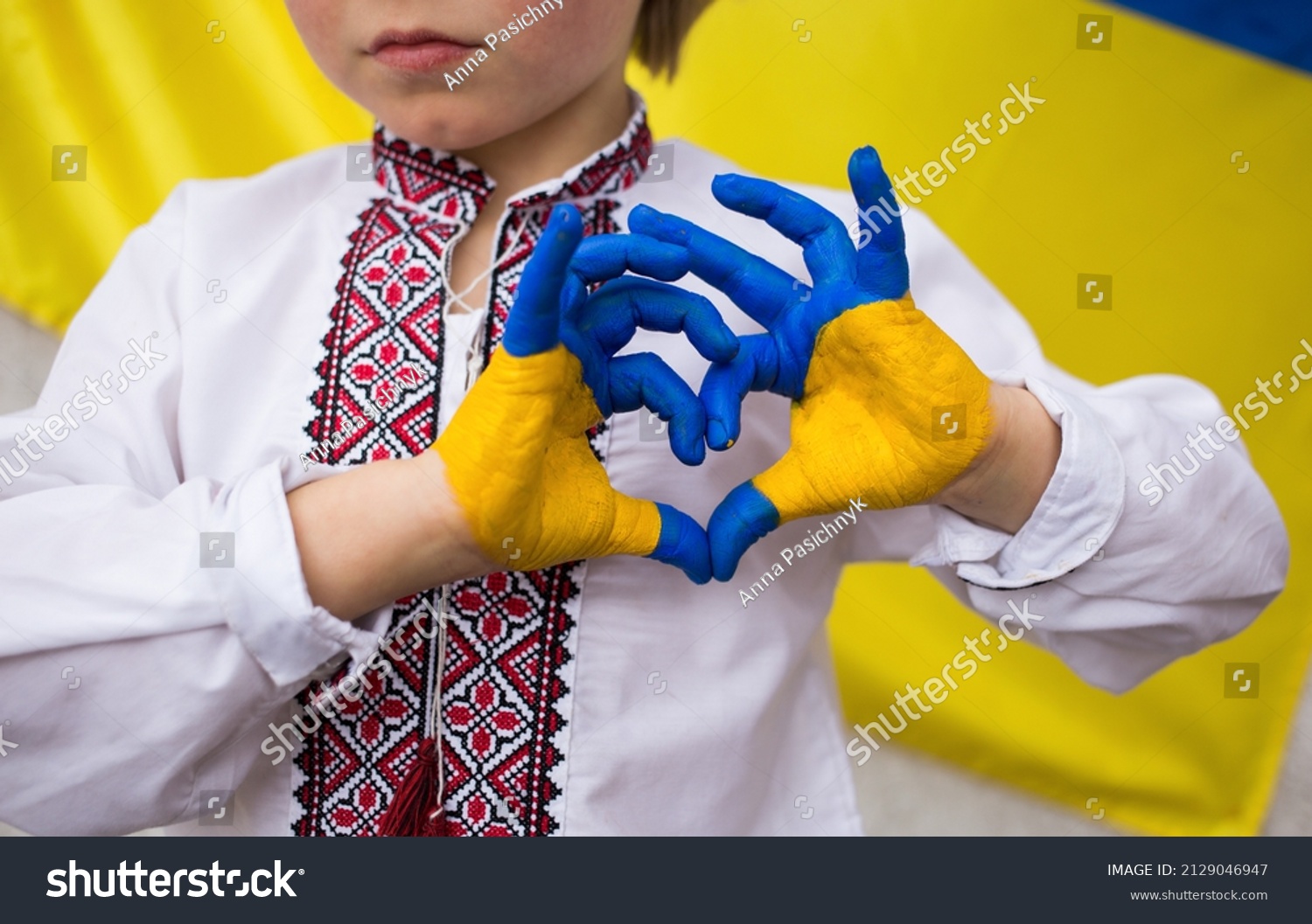 Children against war. Russia's invasion of Ukraine, request for help from world community. child against background of Ukrainian flag with hands in shape of a heart, painted in yellow and blue #2129046947