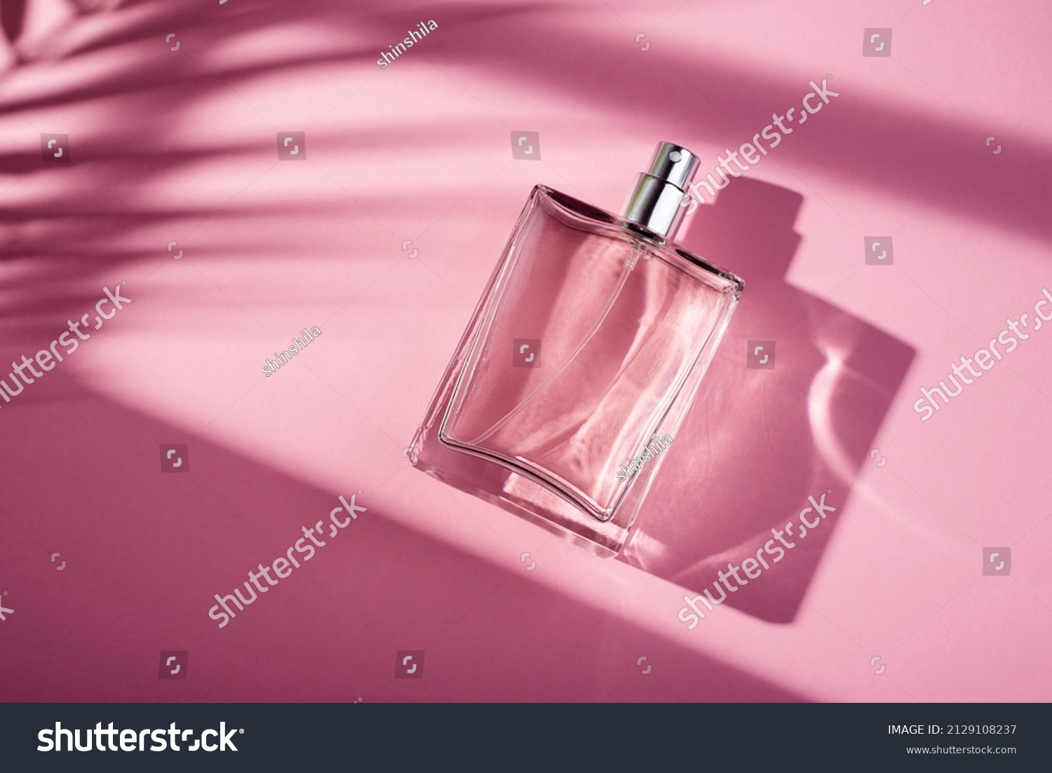 Transparent bottle of perfume on a pink background. Fragrance presentation with daylight. Trending concept in natural materials with window shadow. Women's essence. #2129108237