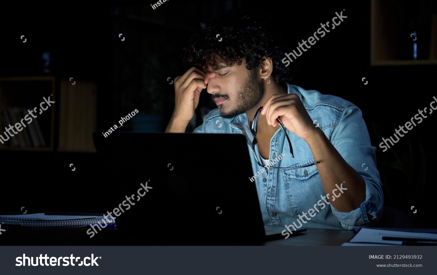 Overworked young indian businessman taking off glasses working late at night. Tired sleepy stressed student holding eyeglasses feeling lack of sleep, having eyestrain problem, using laptop computer. #2129493932