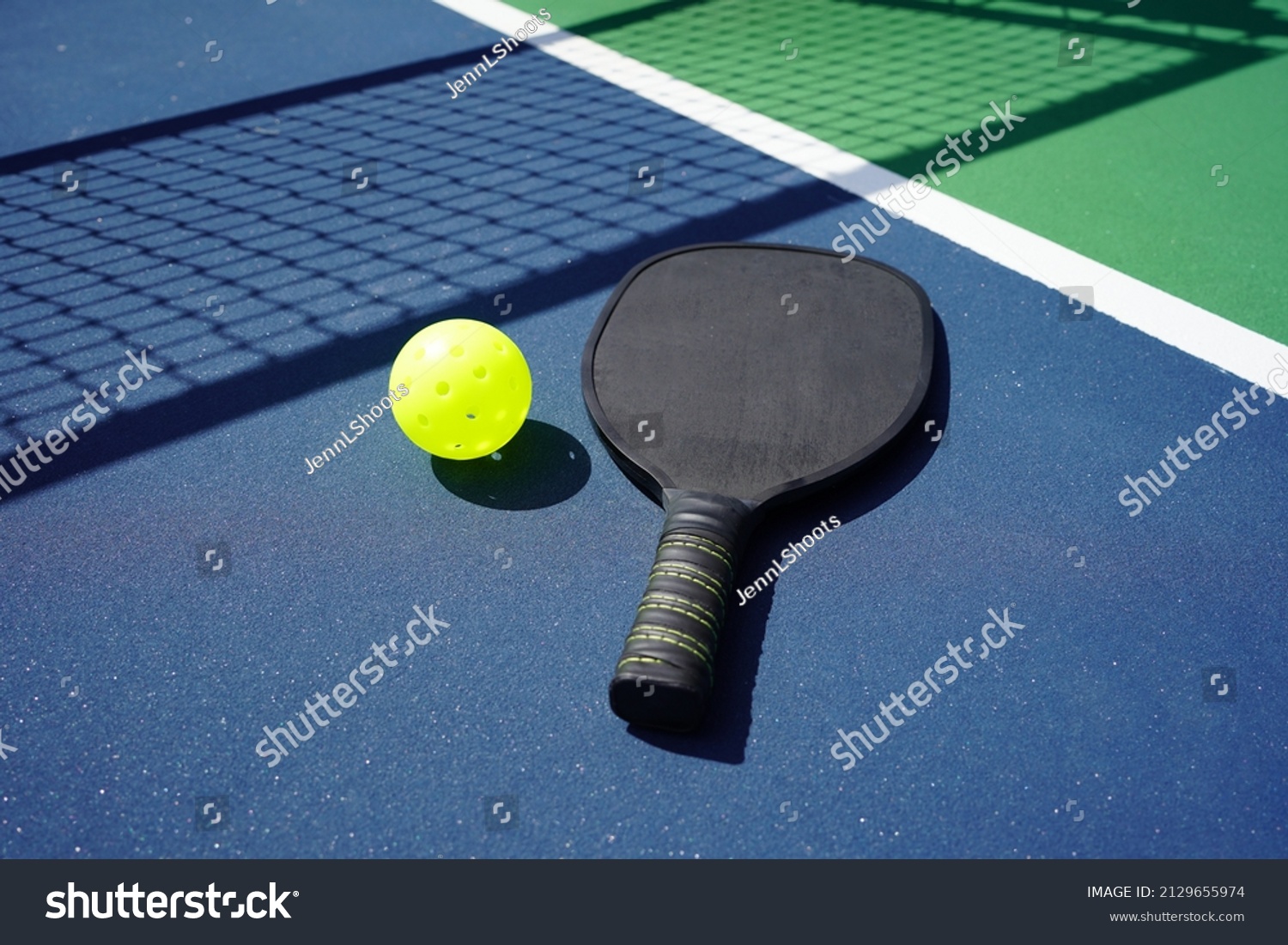 Pickle ball paddle and pickle ball on court with net shadow in background. #2129655974