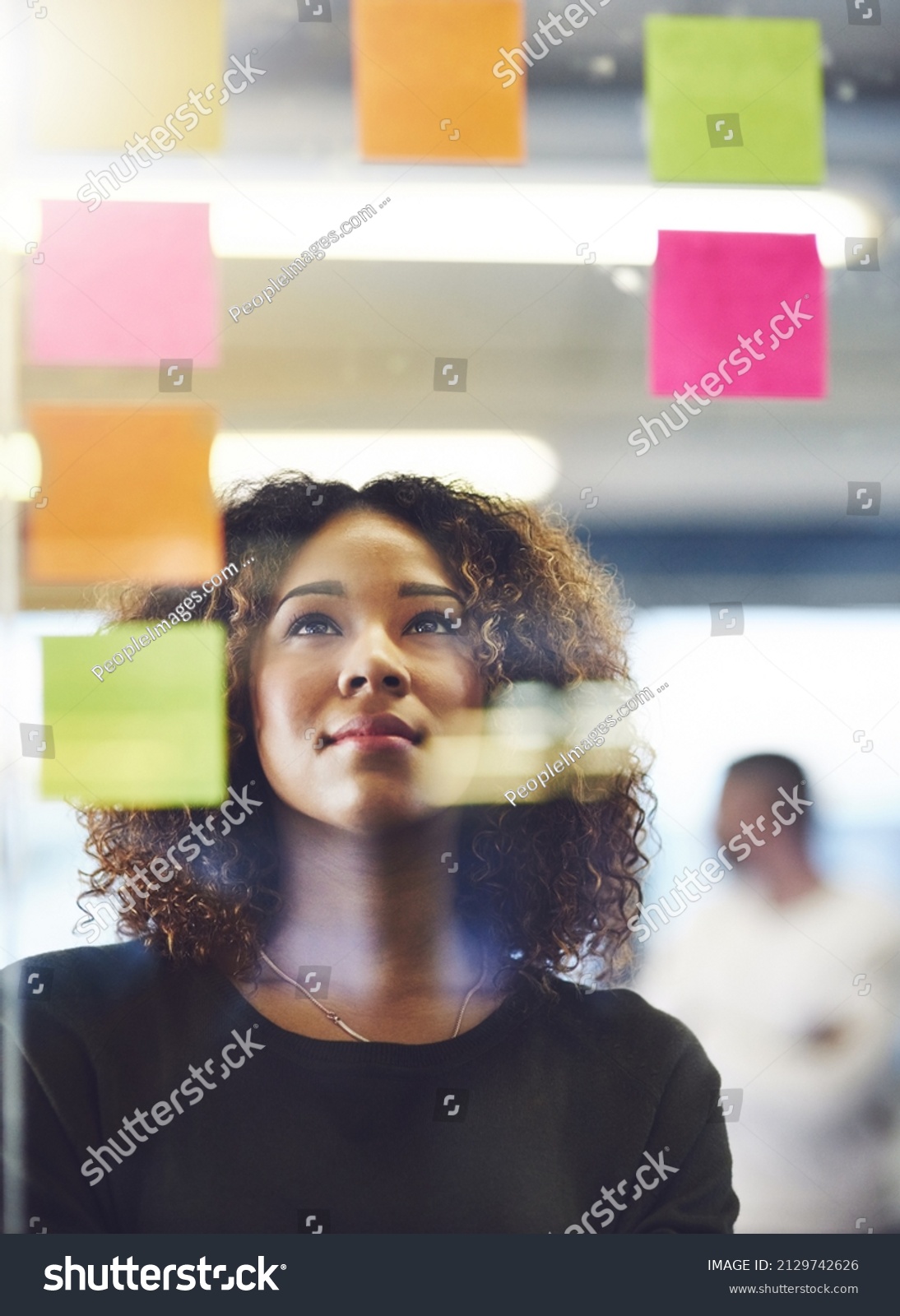 Thinking critically to create success. Shot of a young woman having a brainstorming session with sticky notes at work. #2129742626