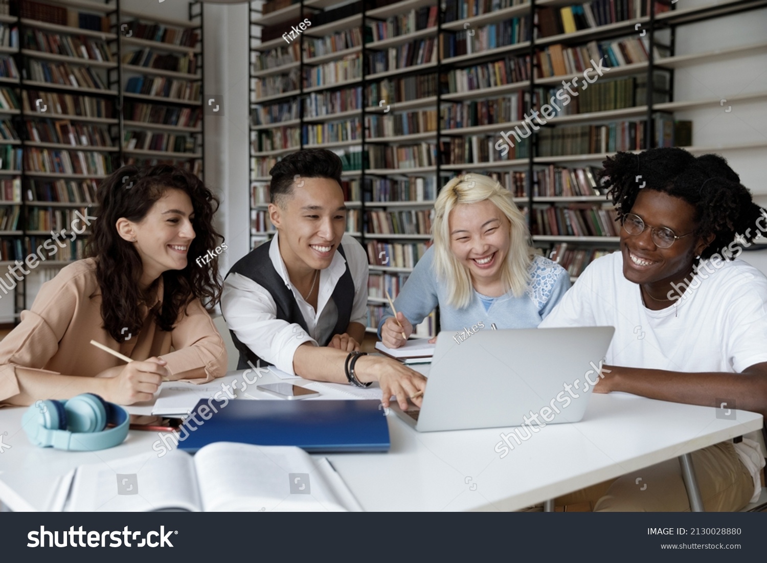 Happy four young multiethnic college students looking at laptop screen, watching educational online lecture or webinar, working on school project, preparing for exams in library, education concept. #2130028880
