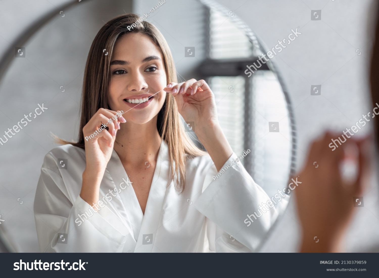 Oral Care. Smiling Young Female Using Dental Floss Near Mirror In Bathroom, Beautiful Millennial Woman Cleansing Teeth, Making Daily Hygiene Routine At Home, Seletive Focus On Reflection #2130379859