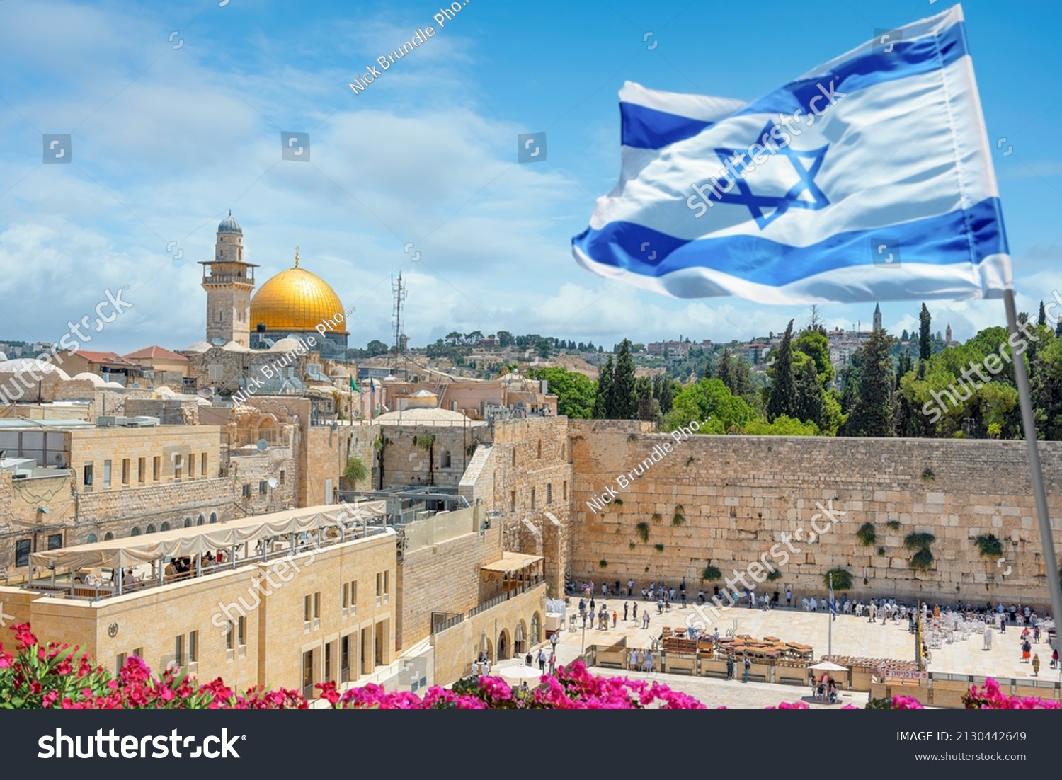 An Israeli flag blows in the wind as jewish orthodox believers read the Torah and pray facing the Western Wall, also known as Wailing Wall in Old City in Jerusalem, Israel.  #2130442649