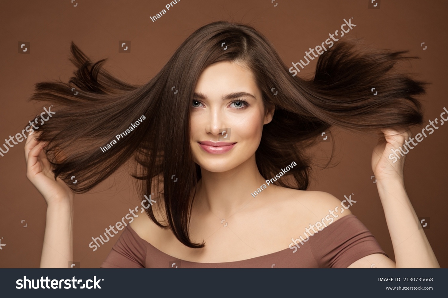 Hair Beauty Model. Brunette Woman with Straight Hairstyle flying on Wind over Dark Beige. Young Smiling Girl with Smooth Skin Make up #2130735668