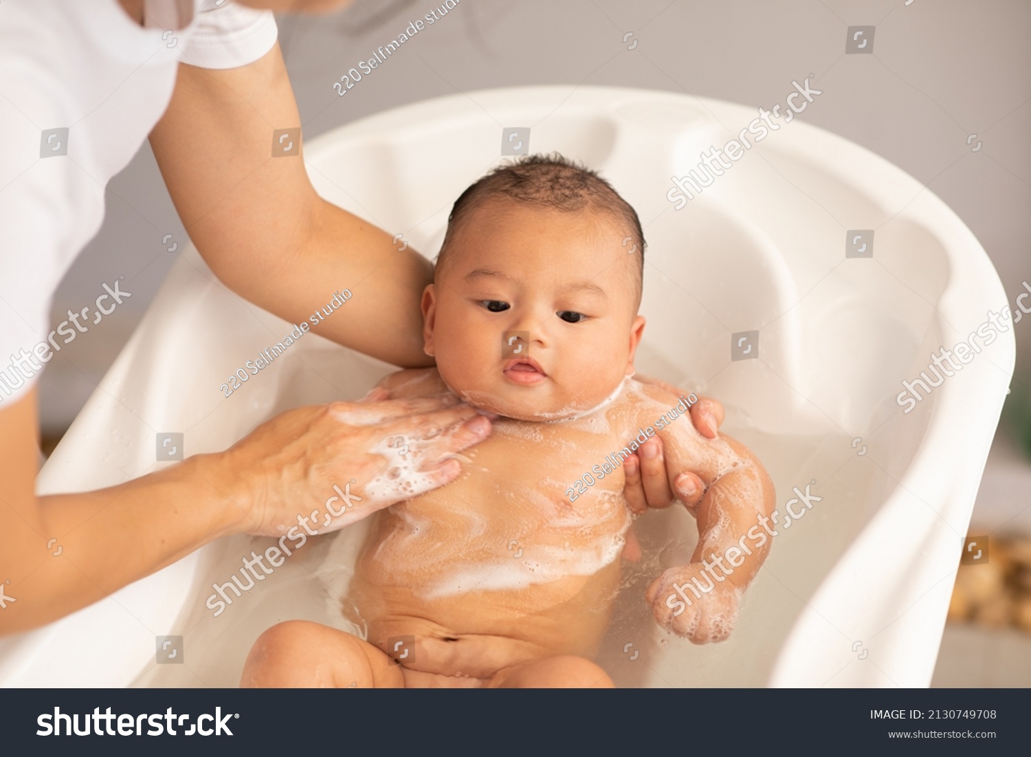 Adorable of asian newborn baby bathing in bathtub.mother bathing her son in warm water.Happy adorable newborn infant smile in tub relax and comfortable.Newborn baby care concept #2130749708