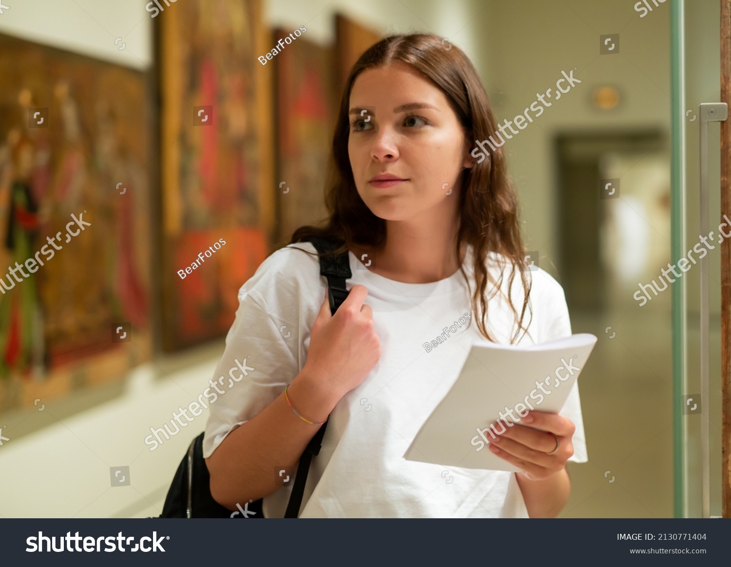 Portrait of a confident girl with an information booklet, standing in the hall of the historical museum next to the ..exhibit, located in a glass cabinet #2130771404
