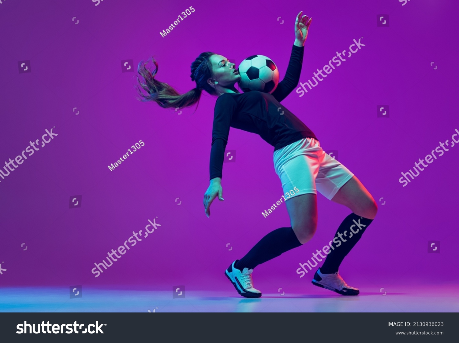 Emotive girl, female soccer, football player in motion, action isolated on purple studio background in neon light. Concept of sport, action, motion, fitness, team, achievements and goals #2130936023