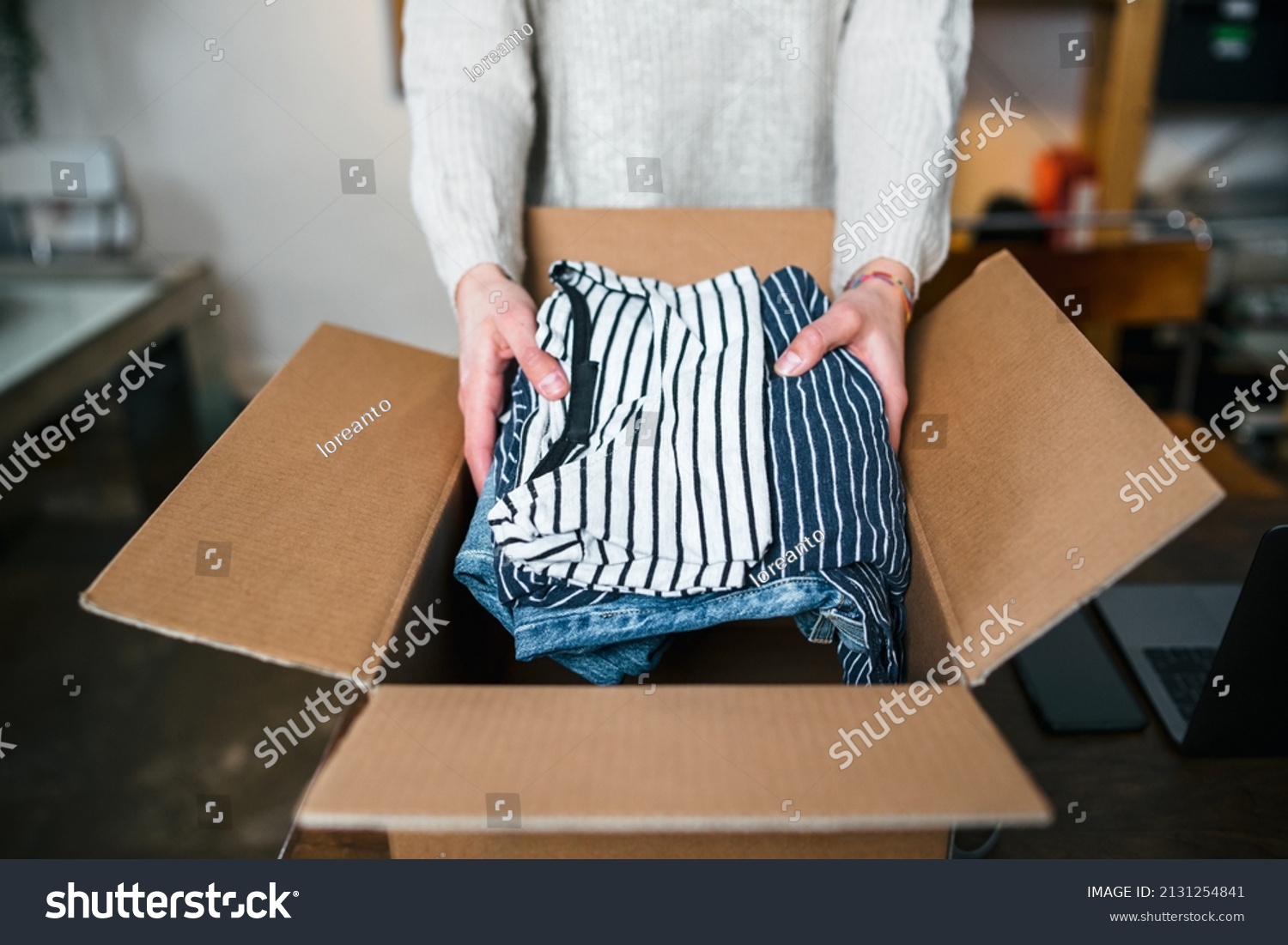 Business woman prepares a package in a cardboard box for shipping with clothes from her online store - Millennial sells second-hand used dresses in her home - Start up concept #2131254841