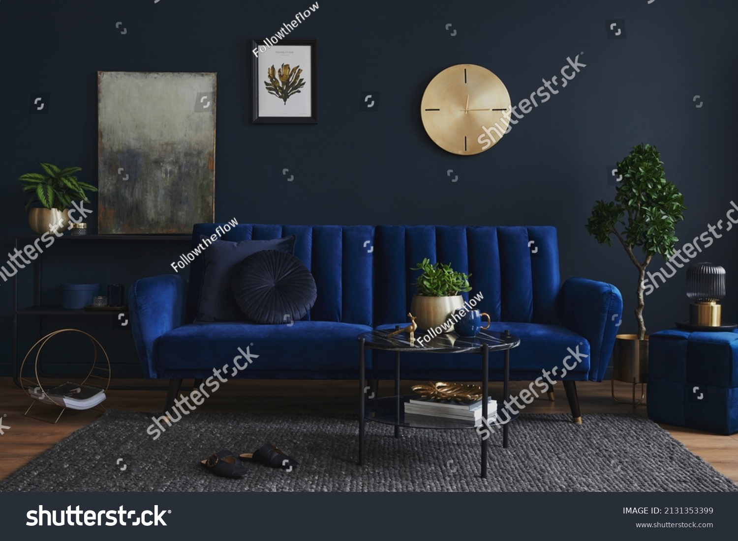 Creative compositon of modern living room interior design with glamour blue sofa, metal shelf, coffee table and elegant home accessories. Dark blue wall. Home staging. Template. Copy space. #2131353399