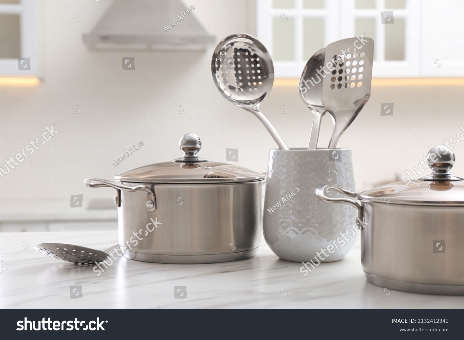 Stainless steel pots and kitchen utensils on white table indoors #2132412341