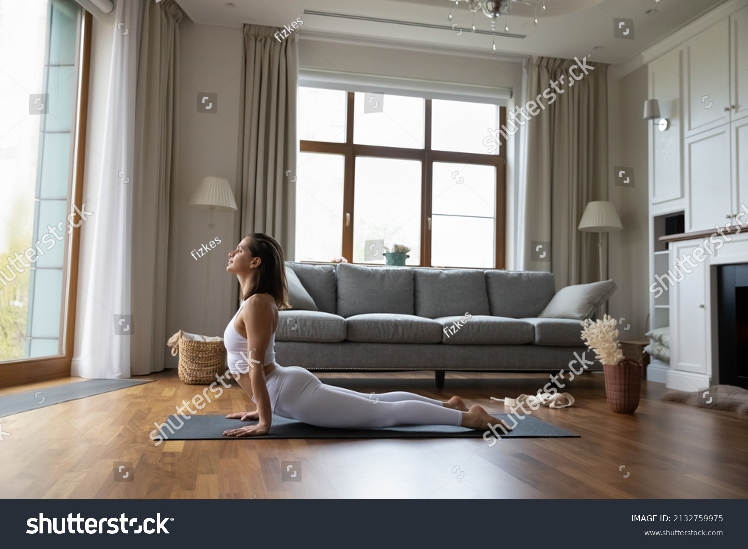 Young sporty yogini woman in fashion comfy white sportswear practicing yoga asanas at home, doing Upward Facing Dog exercise, full-length. Strengthens back muscles, lengthens spine. Training concept #2132759975