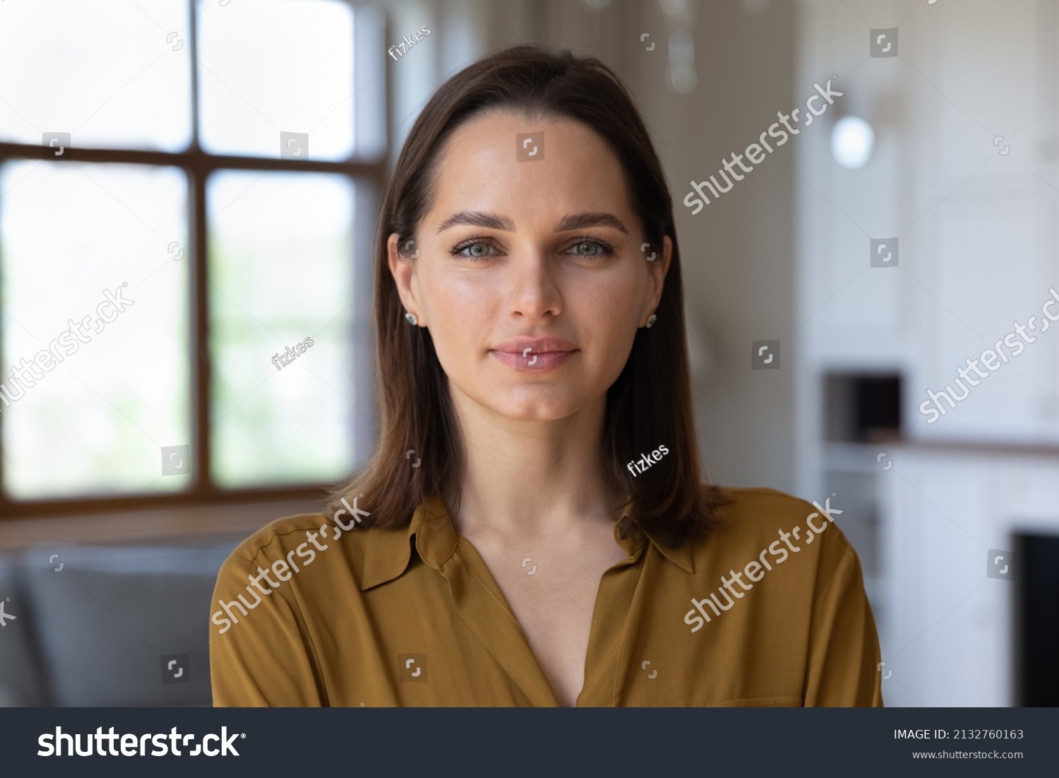Head shot beautiful young 30s female standing in fashionable living room alone pose looking at camera. Homeowner or apartment renter person, pretty housewife portrait, natural womens beauty concept #2132760163
