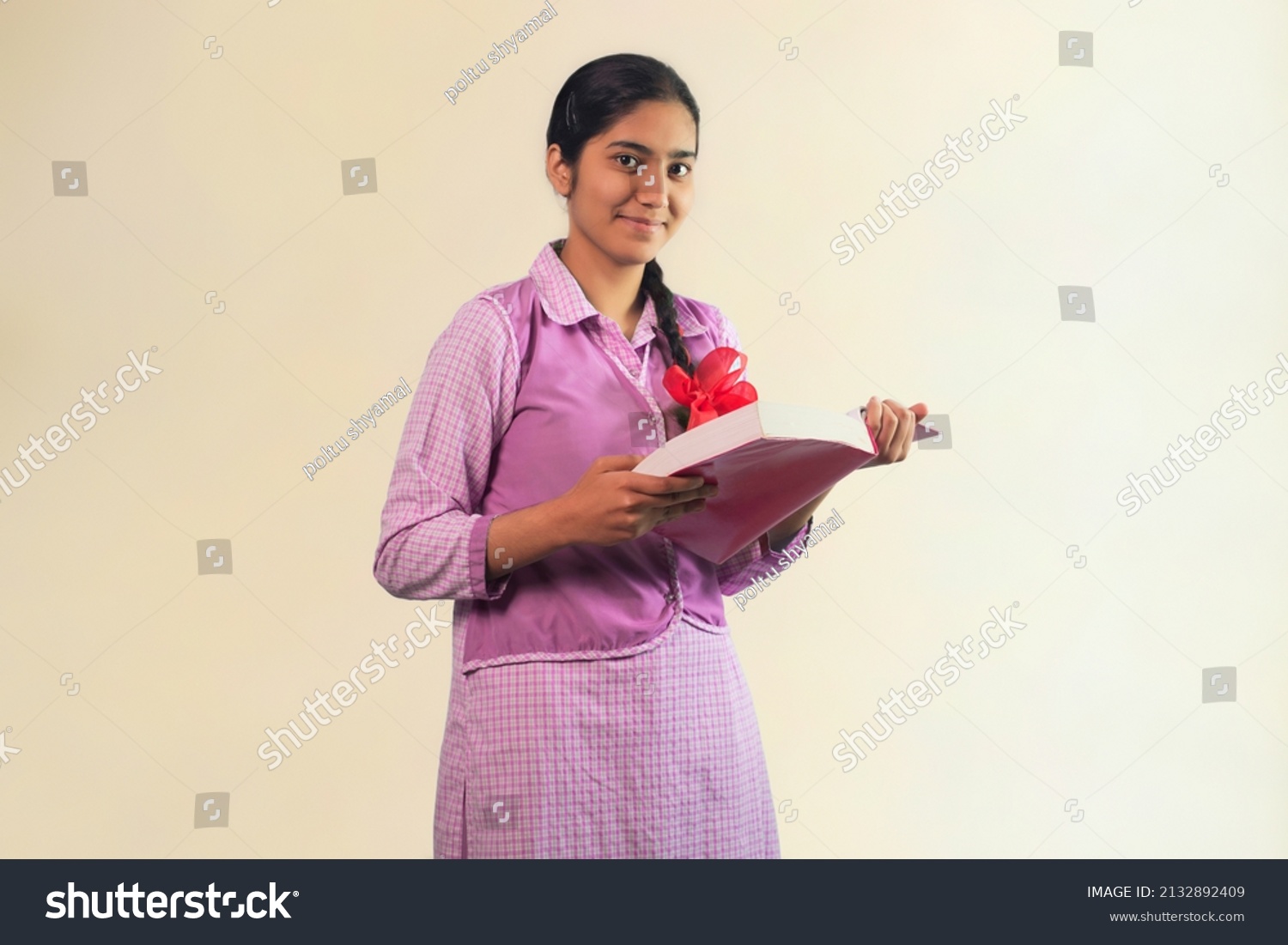 A school girl looking at camera with smile while holding book in her hand #2132892409