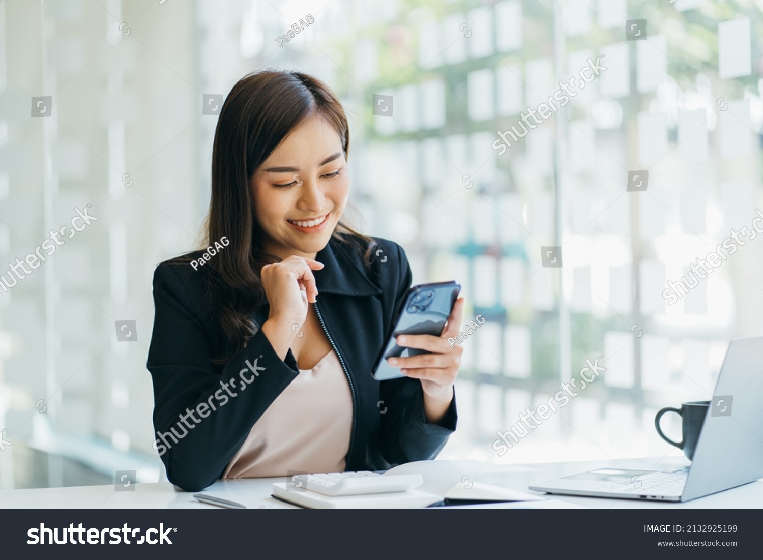 Asian businesswoman in formal suit in office happy and cheerful during using smartphone and working #2132925199