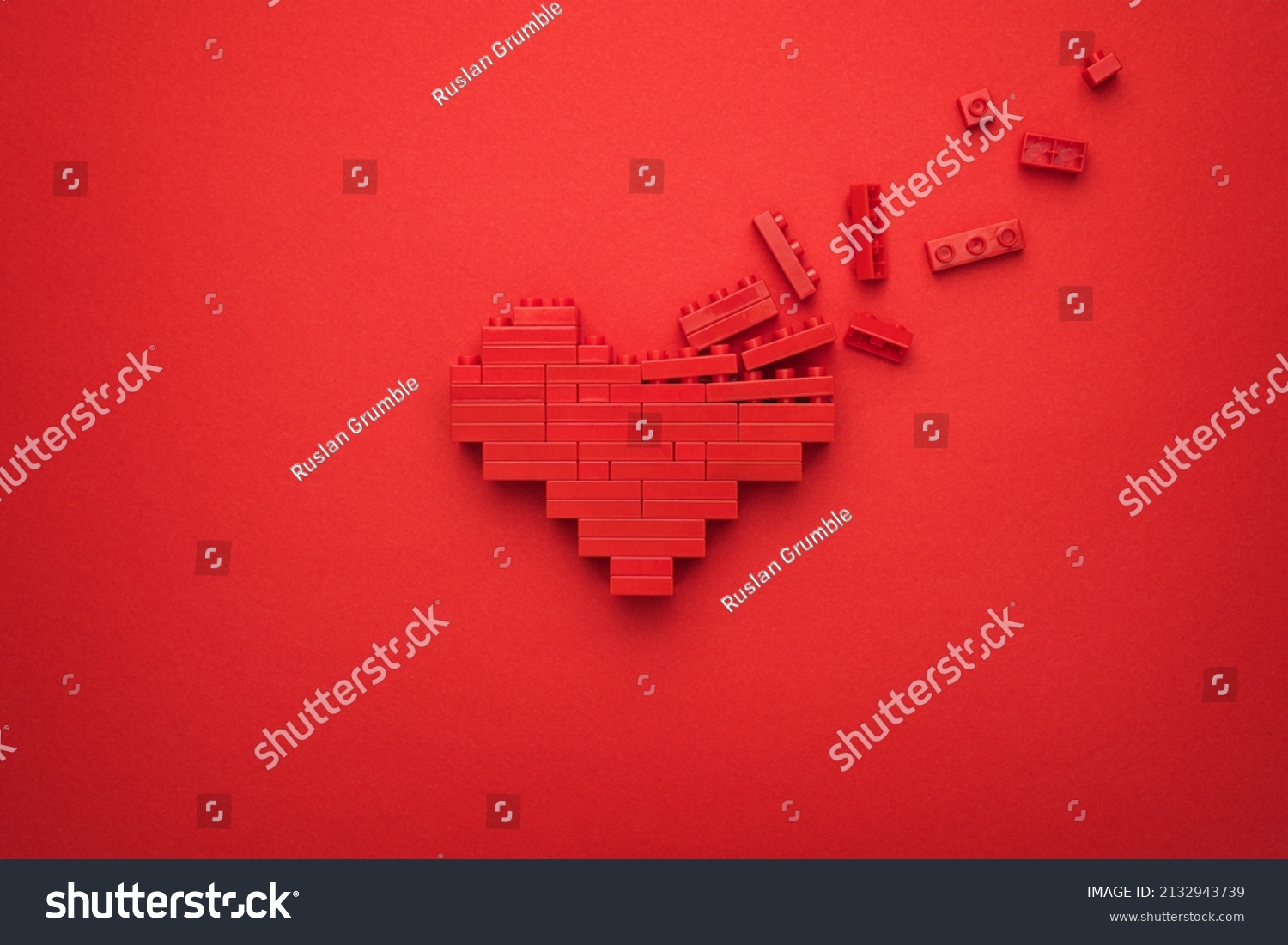Red falling apart heart symbol made of plastic building blocks. Flat lay image of breaking down like button on red background. Minimalist photo of stylized dissolving love symbol. #2132943739