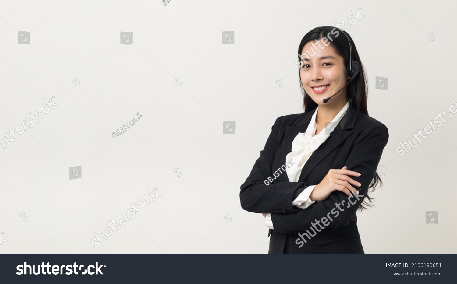 Happy young asian business woman call centre. Welcome female operator put on smalltalk headphone standing on isolated white background. #2133193651