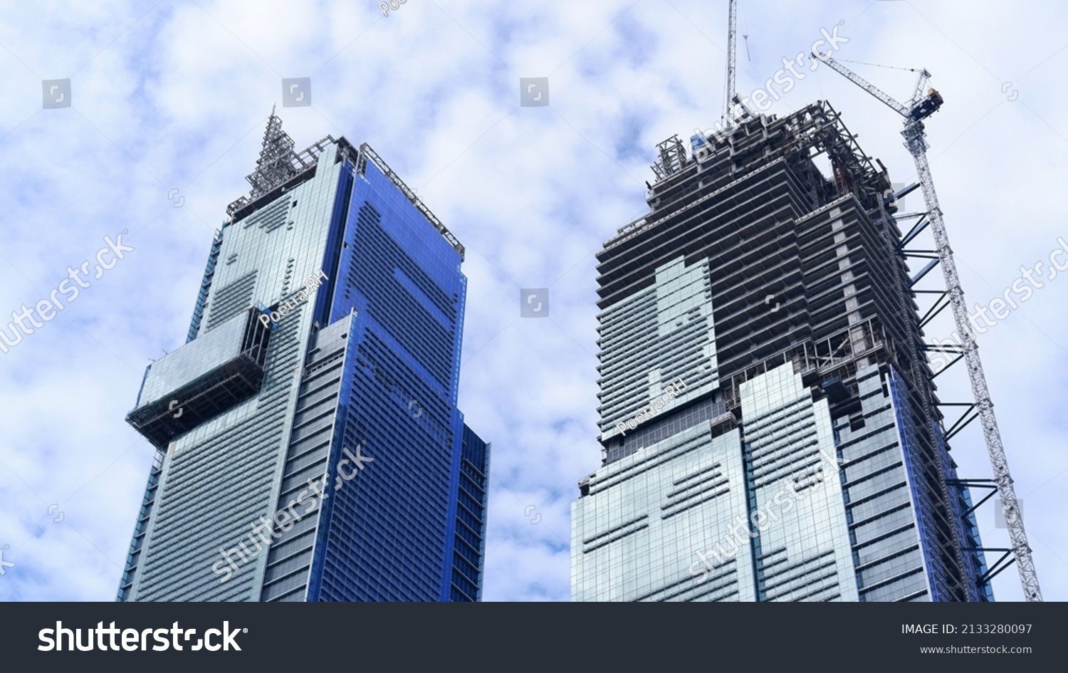 Skyscraper building under construction with tower crane and blue sky background  #2133280097