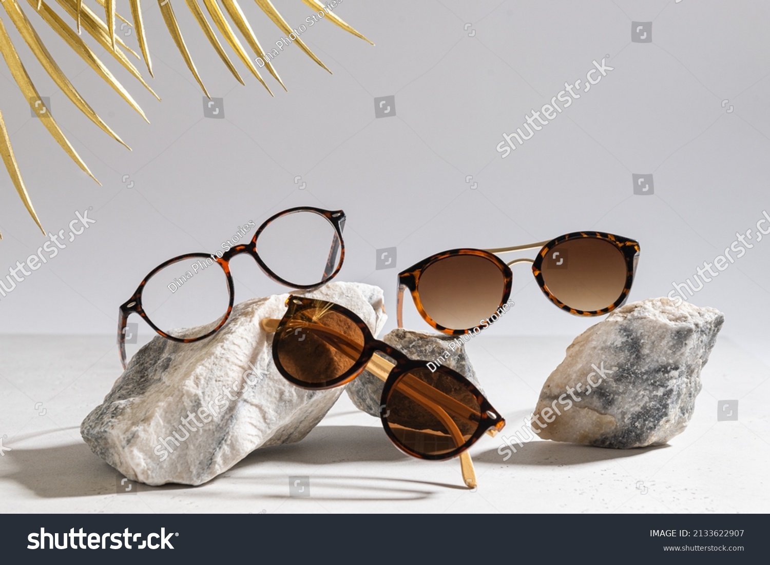 Sunglasses and glasses sale concept. Trendy sunglasses on gray background with golden palm leaves. Trendy Fashion summer accessories. Copy space for text. Summer sale. Optic store discount poster #2133622907
