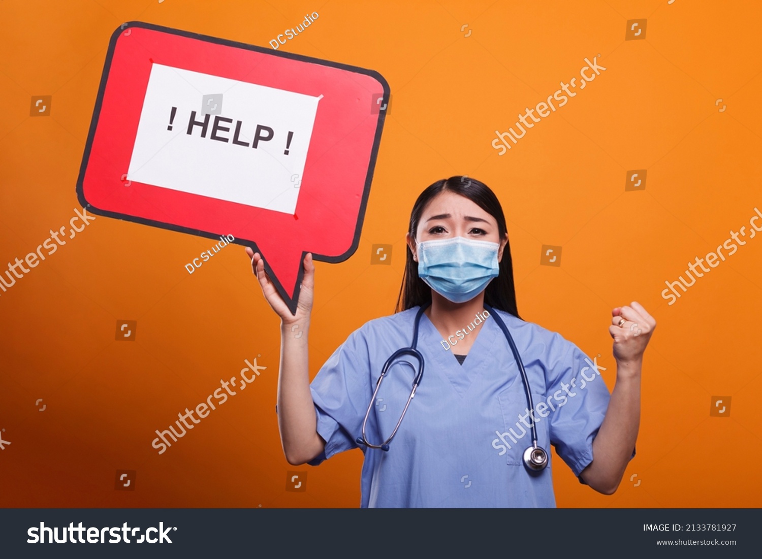 Young adult hospital nurse holding cardboard speech bubble sign while wearing stethoscope and virus protection facemask. Worried medical staff worker wearing medical instrument and asking for help. #2133781927