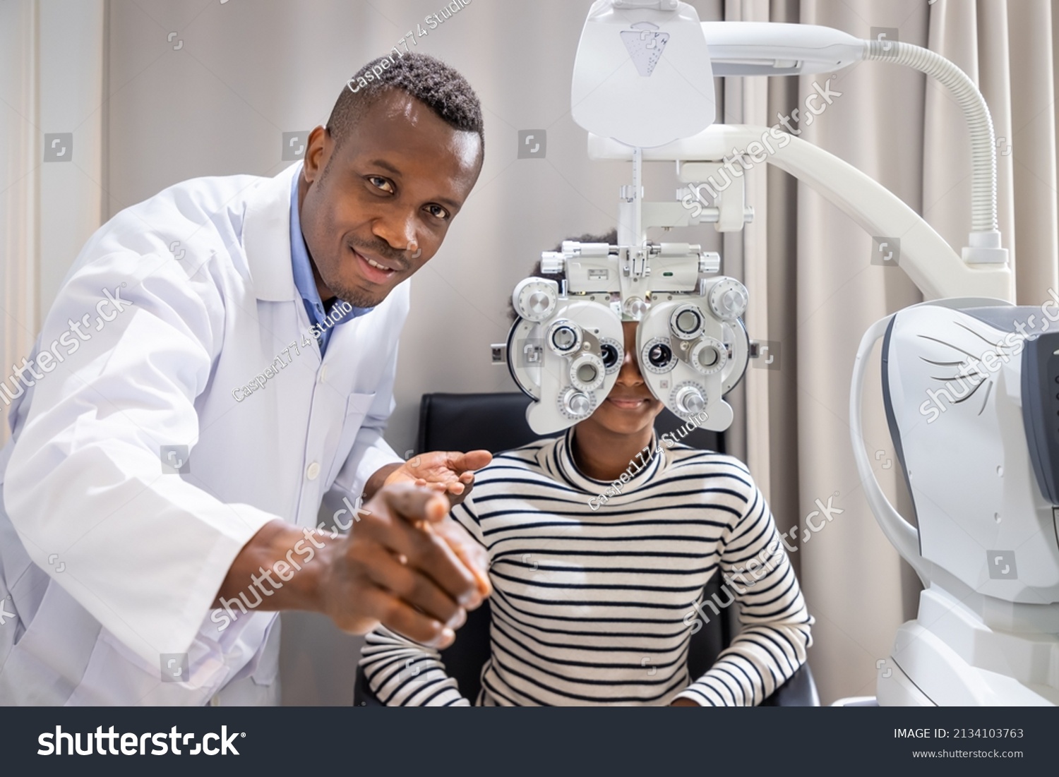 African young woman girl doing eye test checking examination with male man optometrist using phoropter in clinic or optical shop. Eyecare concept. #2134103763