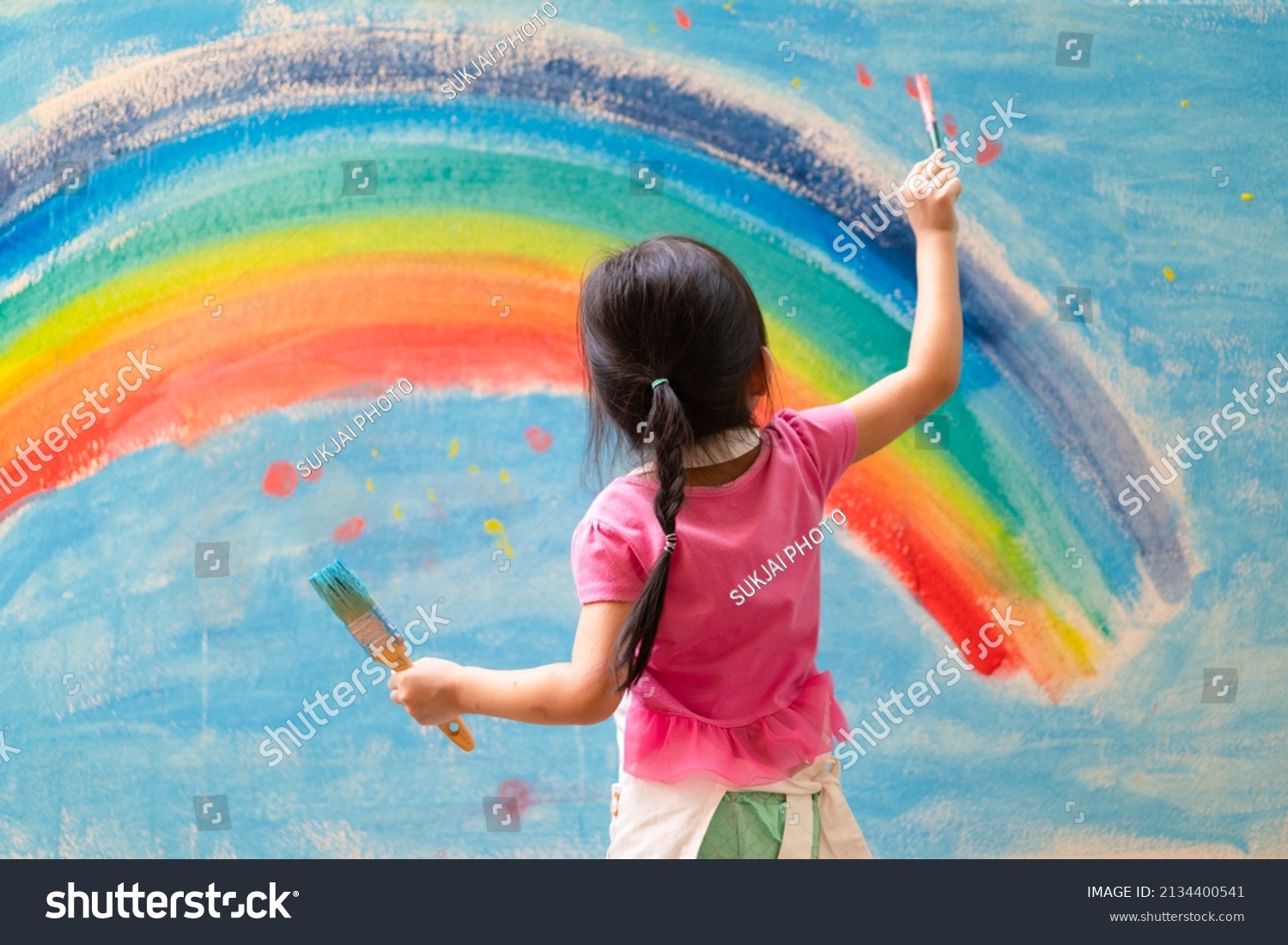 Unidentified little girl is painting the colorful rainbow and sky on the wall and she look happy and funny, concept of art education and learn through play activity for kid development.	 #2134400541