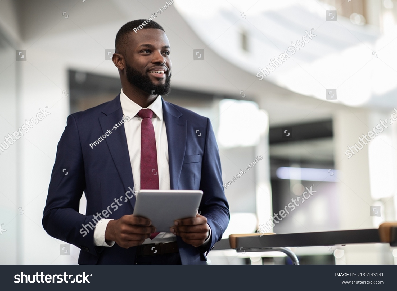 Cheerful young bearded african american man manager walking by office building corridor, holding modern digital tablet, using mobile app for business, looking at copy space and smiling, panorama #2135143141