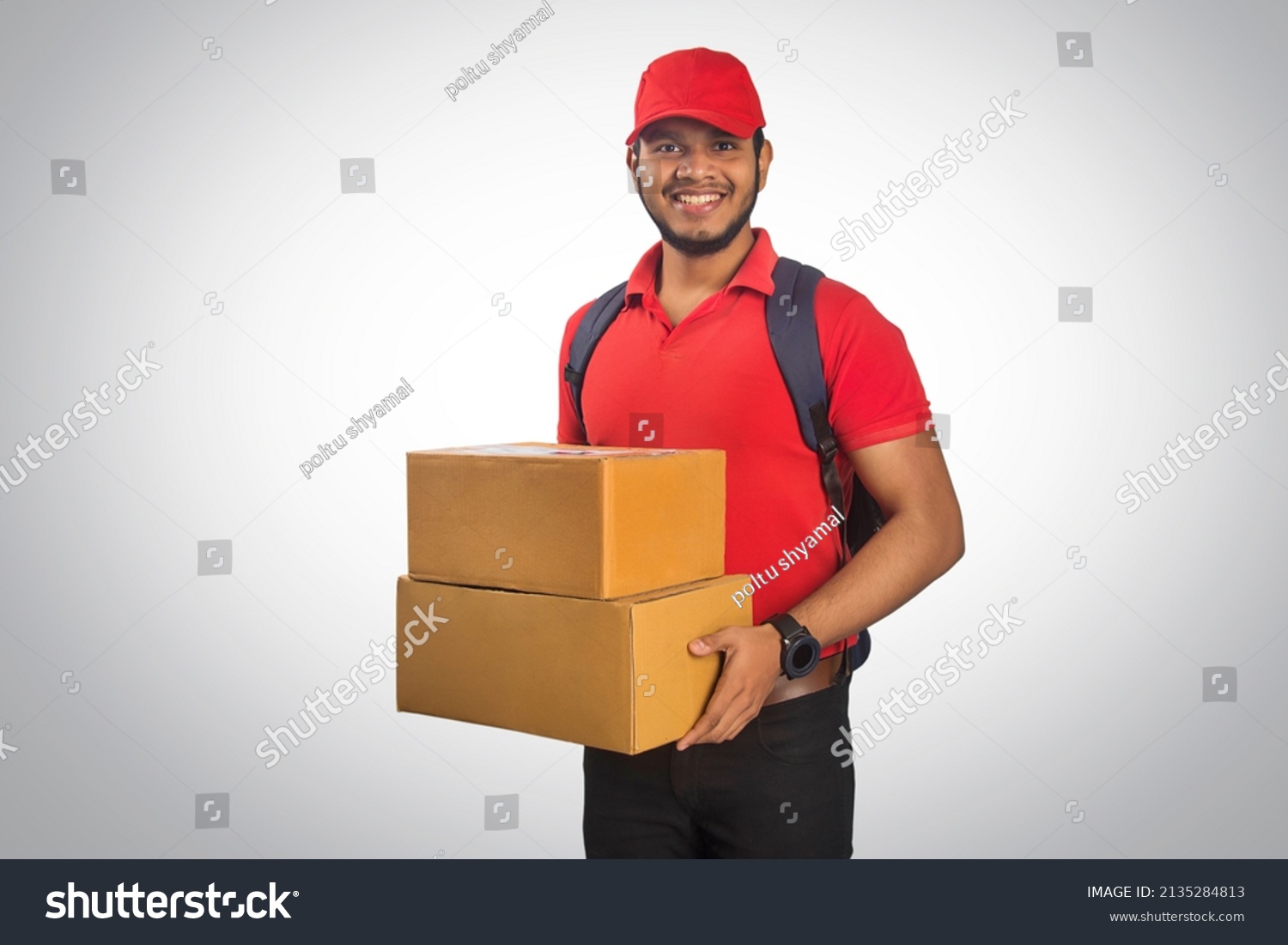 Portrait Of Young Delivery Man Holding Cardboard Box Against Grey Background #2135284813