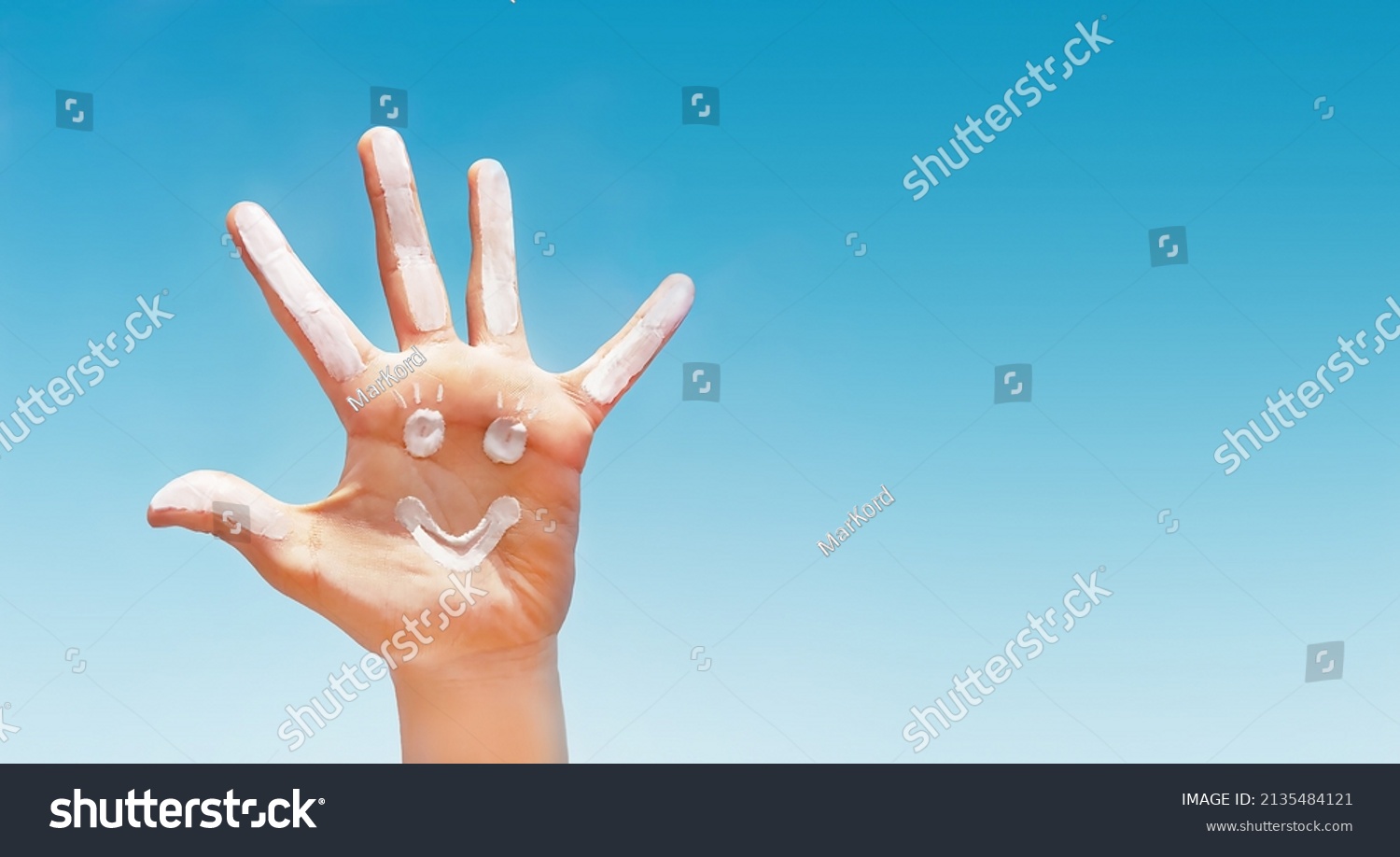 Positive symbol drawing by sunscreen (sun cream, suntan lotion) on caucasian open hand on blue sky background. Concept of protection (safety) from sun, skin care, happy summer vacation. Copy space. 
 #2135484121