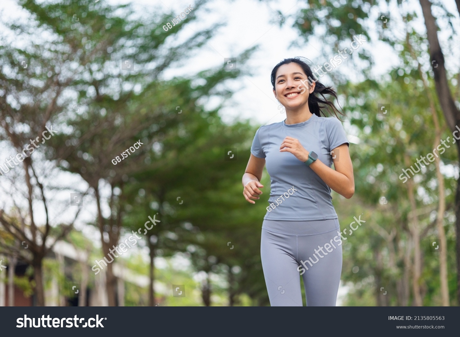 Happy slim woman wearing sportswear jogging in the city at sunrise. Young beautiful asian female in sports bra running outdoor. Workout exercise in the morning. Healthy and active lifestyle concept. #2135805563