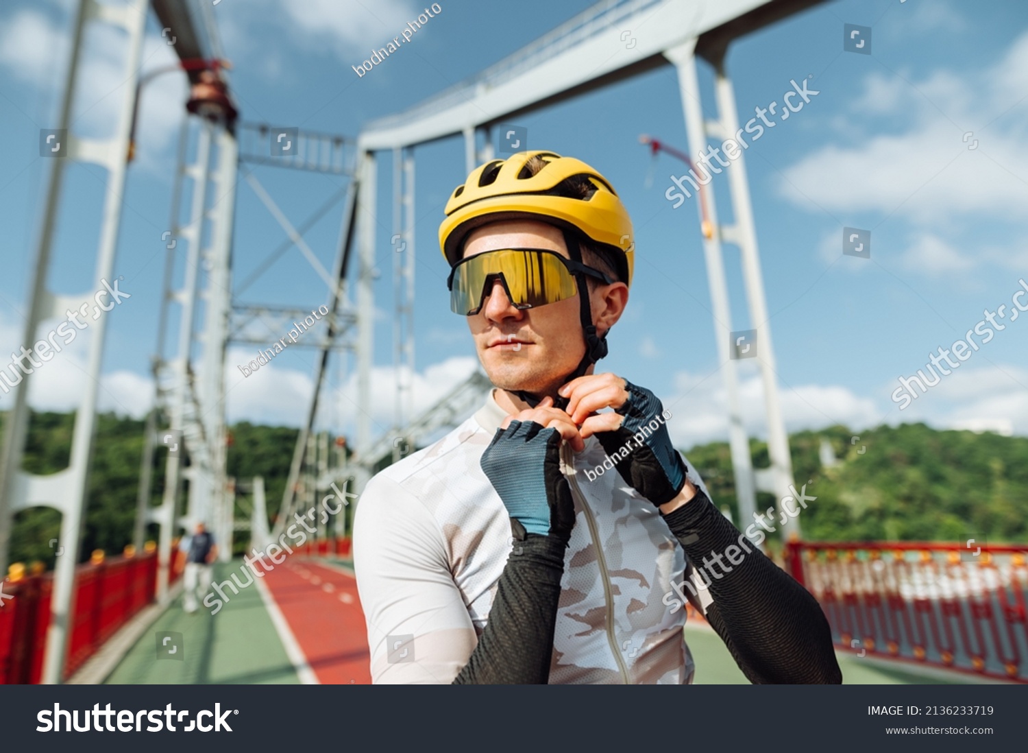 Portrait of a handsome male cyclist in a helmet and sporty outfit on the background of the bridge, looks away with a serious face and wears protection #2136233719