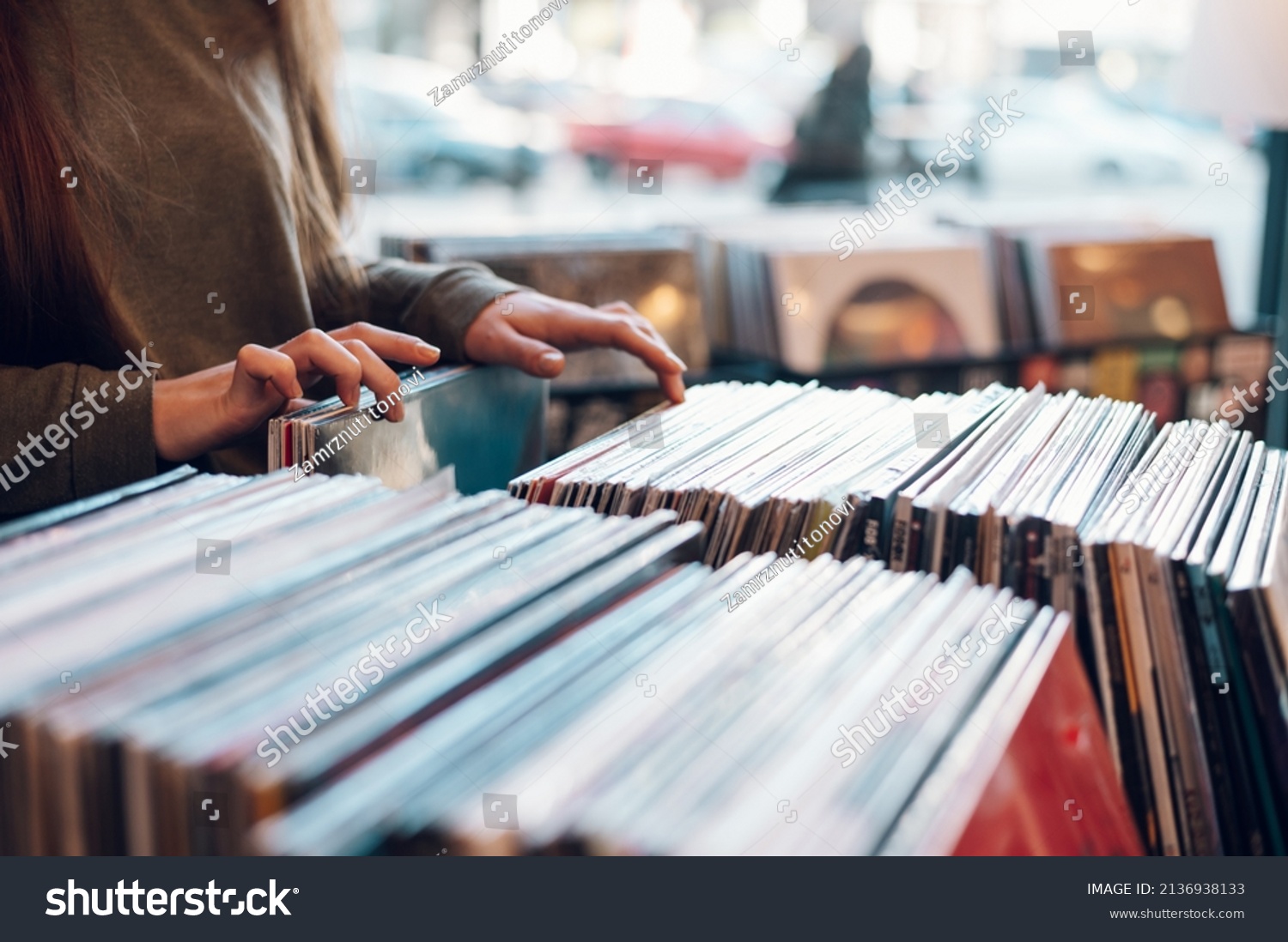 Close up of a woman hands choosing vinyl record in music record shop. Music addict concept. Old school classic concept. Focus on the hands and a vinyl record. #2136938133