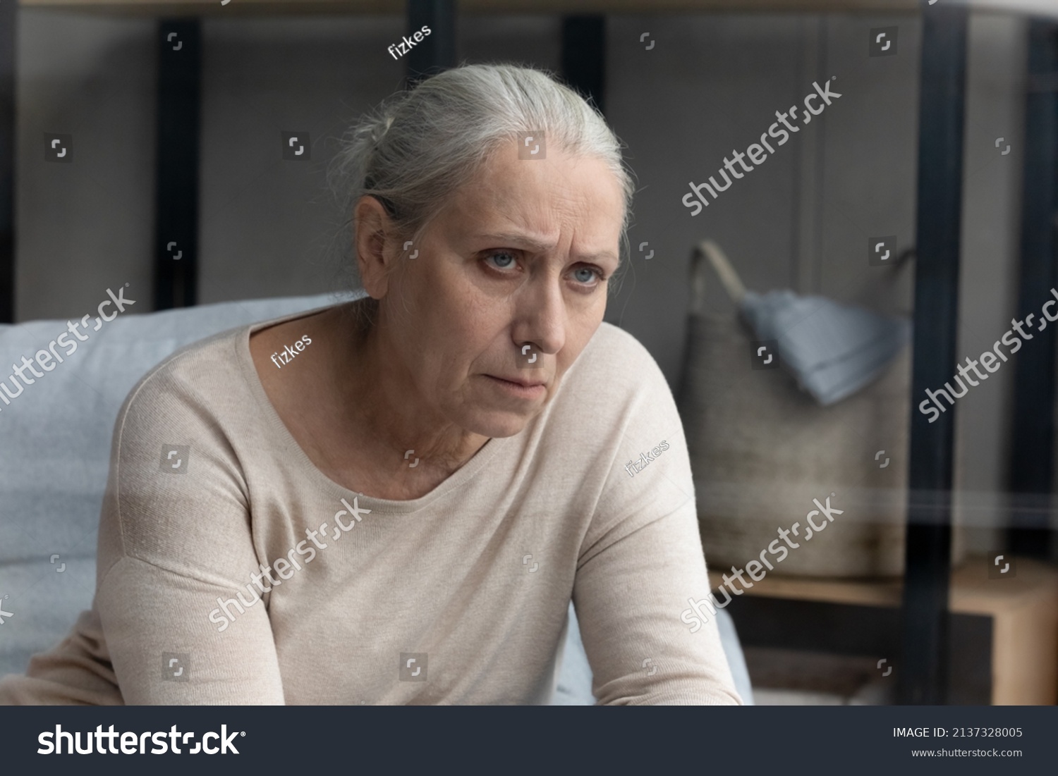 Pessimistic aged woman sits on sofa in living room feels hurt and lonely, lost in sad thoughts related to senile disease, mental disorder or dementia. Life troubles, solitude of older citizen concept #2137328005