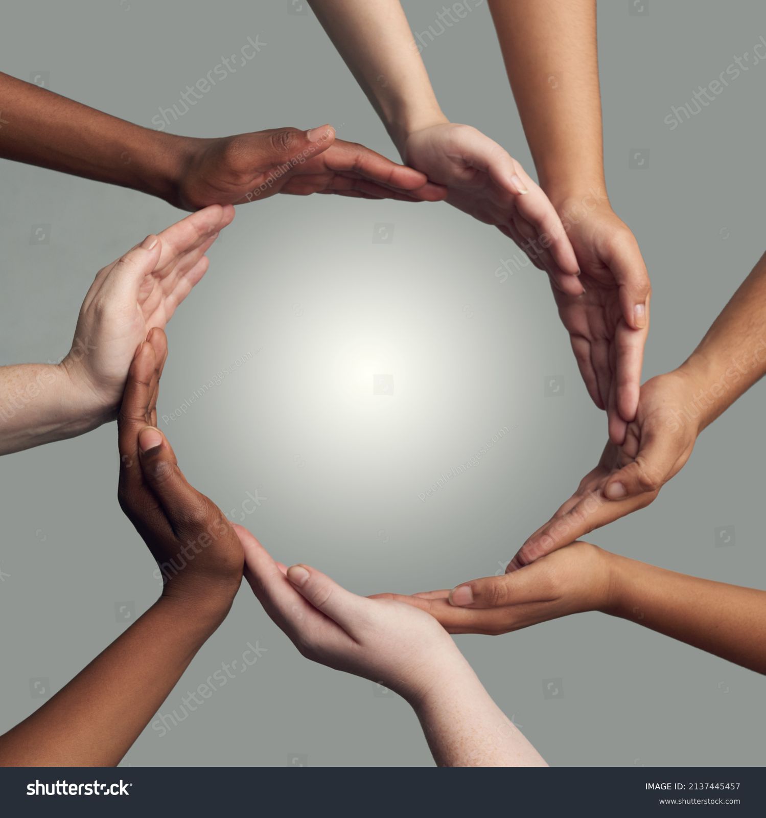 Coming together to form one. Cropped shot of a group of hands linking together to form a circle against a grey background. #2137445457
