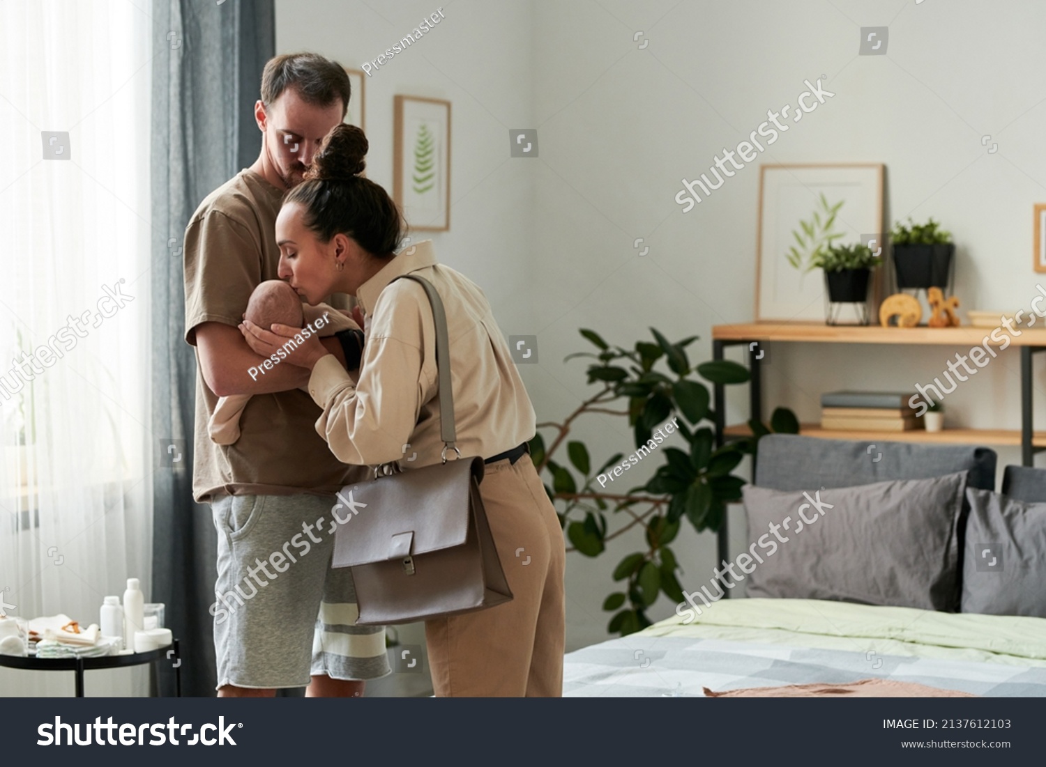 Young affectionate female kissing cute baby son on hand of her husband in the morning while saying goodbye and leaving for work #2137612103