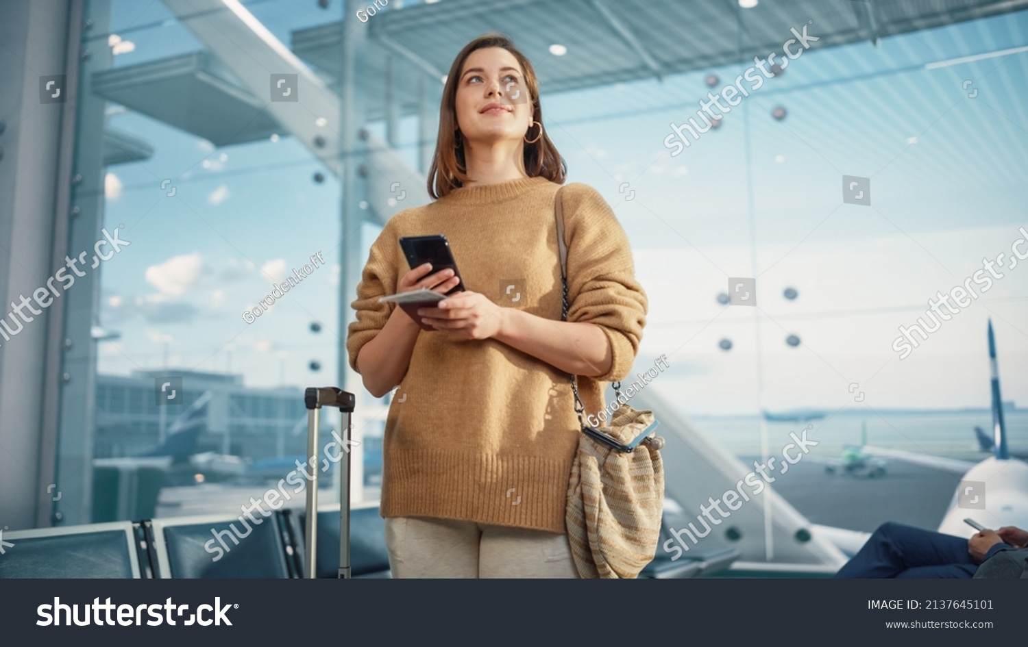 Airport Terminal: Happy Traveling Caucasian Woman Waiting at Flight Gates for Plane Boarding, Uses Mobile Smartphone, Checking Trip Destination on Internet. Smiling White Female in Airline Hub #2137645101