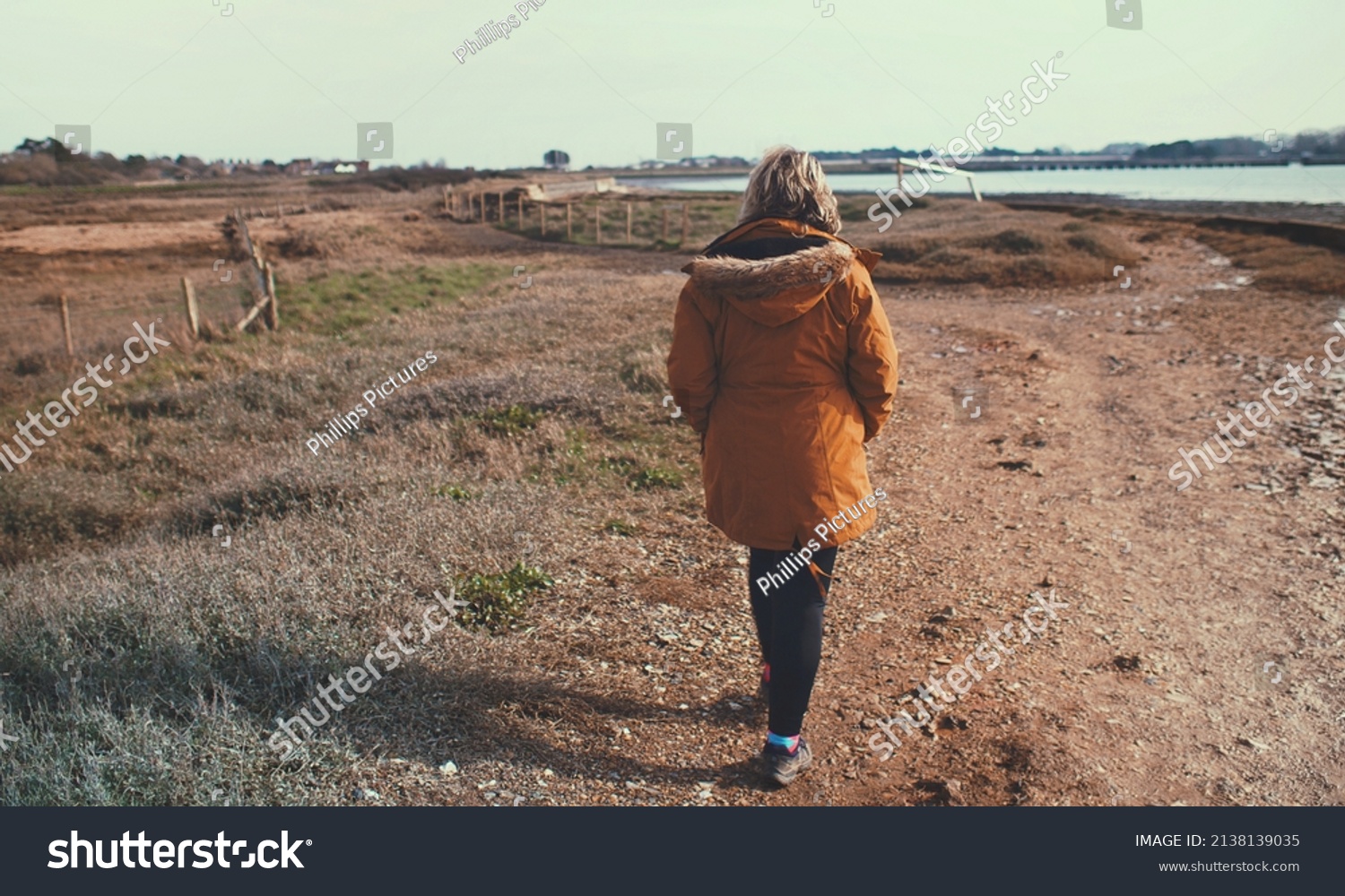 Woman walking along shoreline next to a river #2138139035