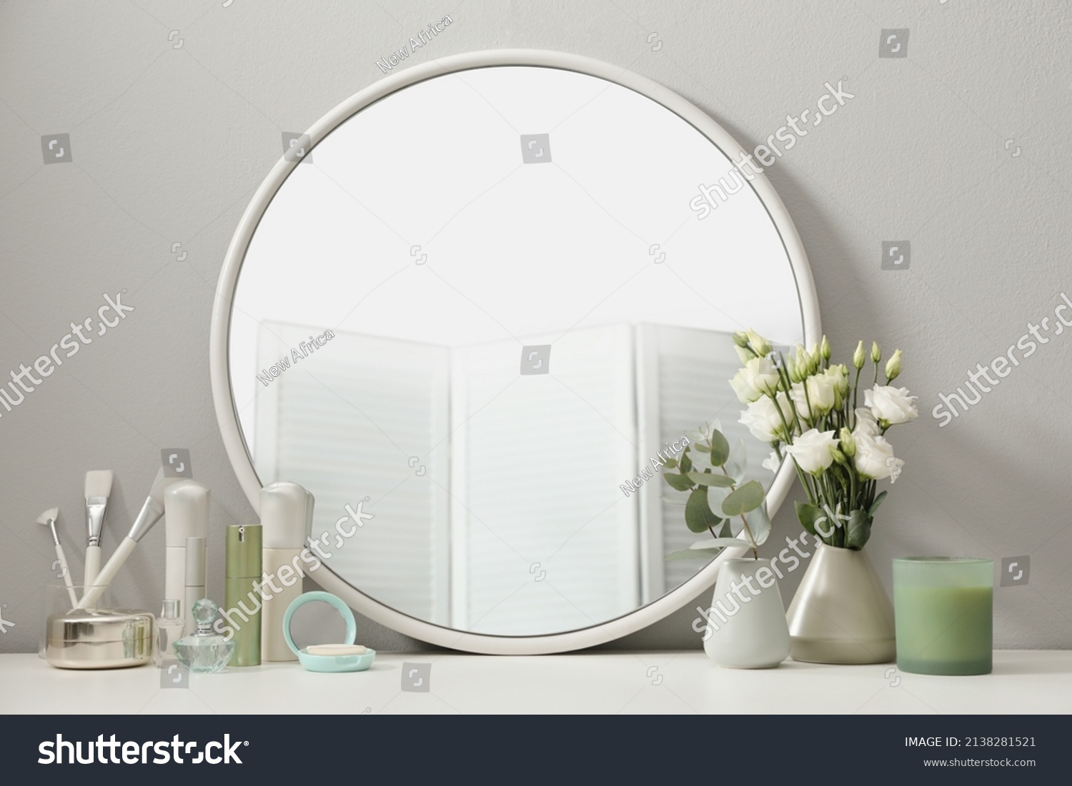 Stylish round mirror on dressing table with cosmetic products and flowers #2138281521