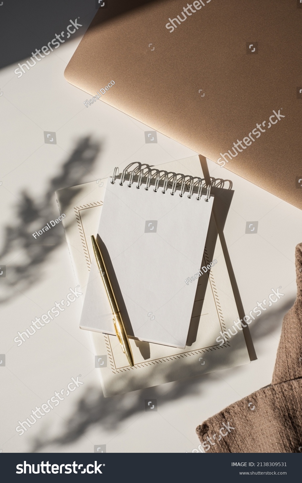 Spiral flip notebook with blank copy space, pen, laptop computer in flowers sunlight shadow on white table. Aesthetic bohemian minimalist workspace. Artist, writer template #2138309531
