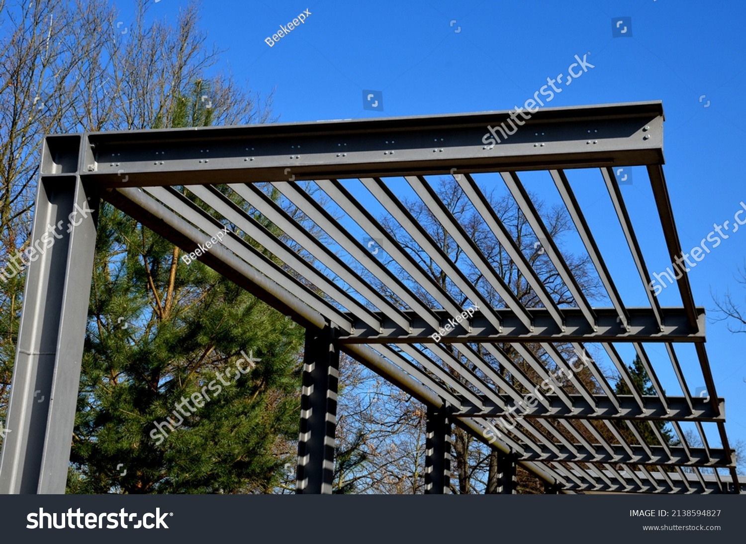 metal construction of the bus stop, gazebo pergola shelter. The roof is designed for climbing plants. L-painted beams and L-shaped ribs shading blinds with stripes on promenade in the park, sky,  blue #2138594827