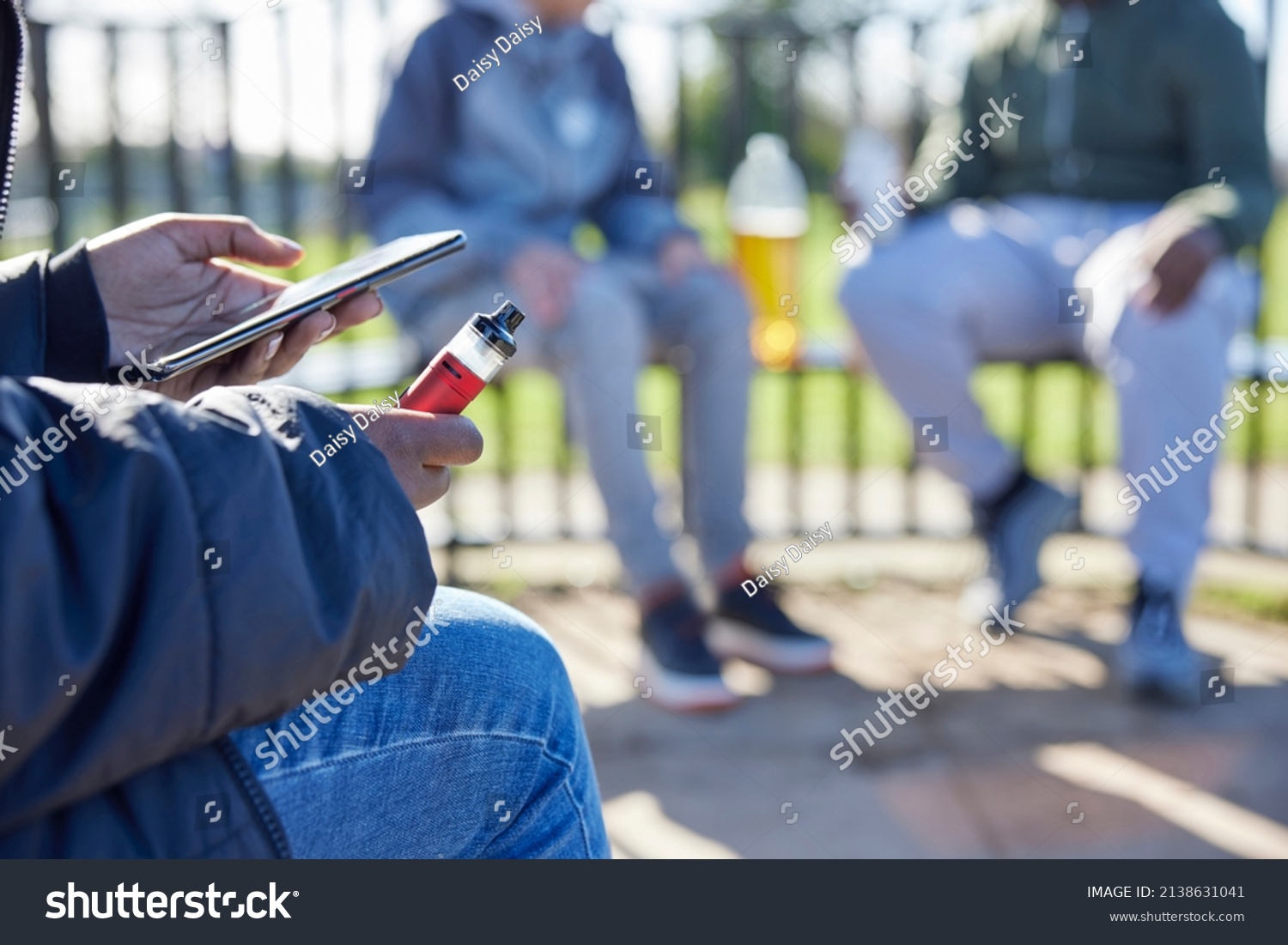 Close Up Of Teenagers With Mobile Phone Vaping and Drinking Alcohol In Park #2138631041