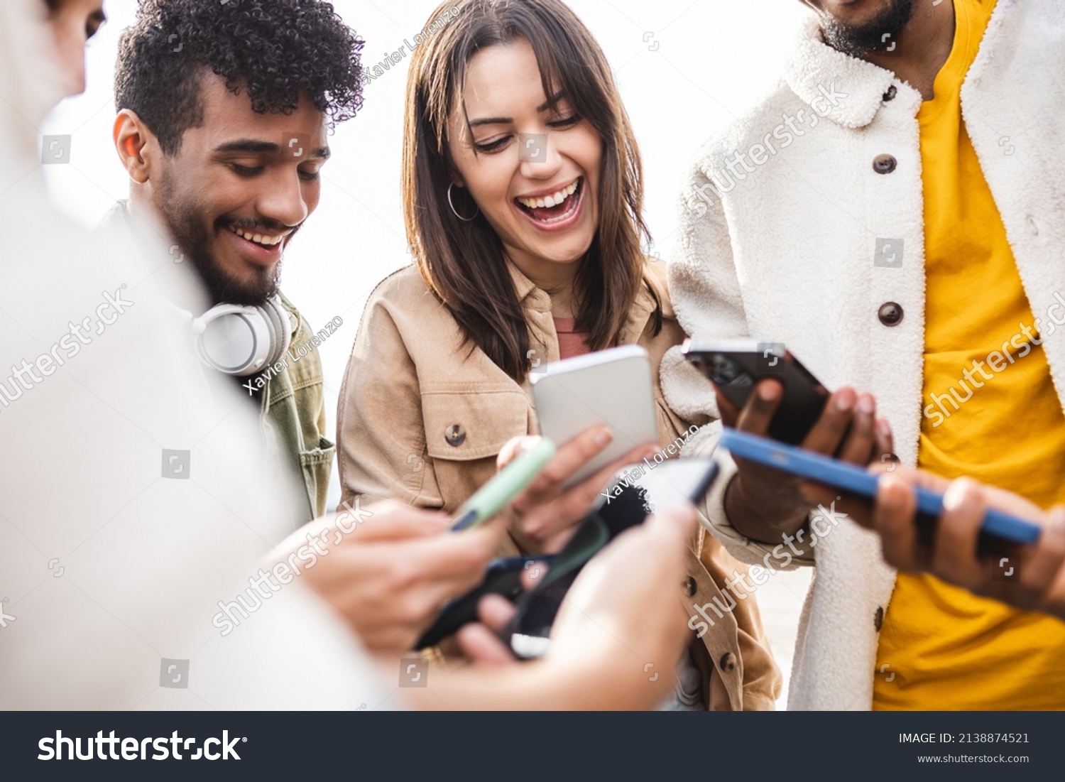 Young group of people using mobile phone outdoors - Addicted diverse friends holding smartphones sharing social media content on digital network app - Youth and technology concept - Focus woman face #2138874521