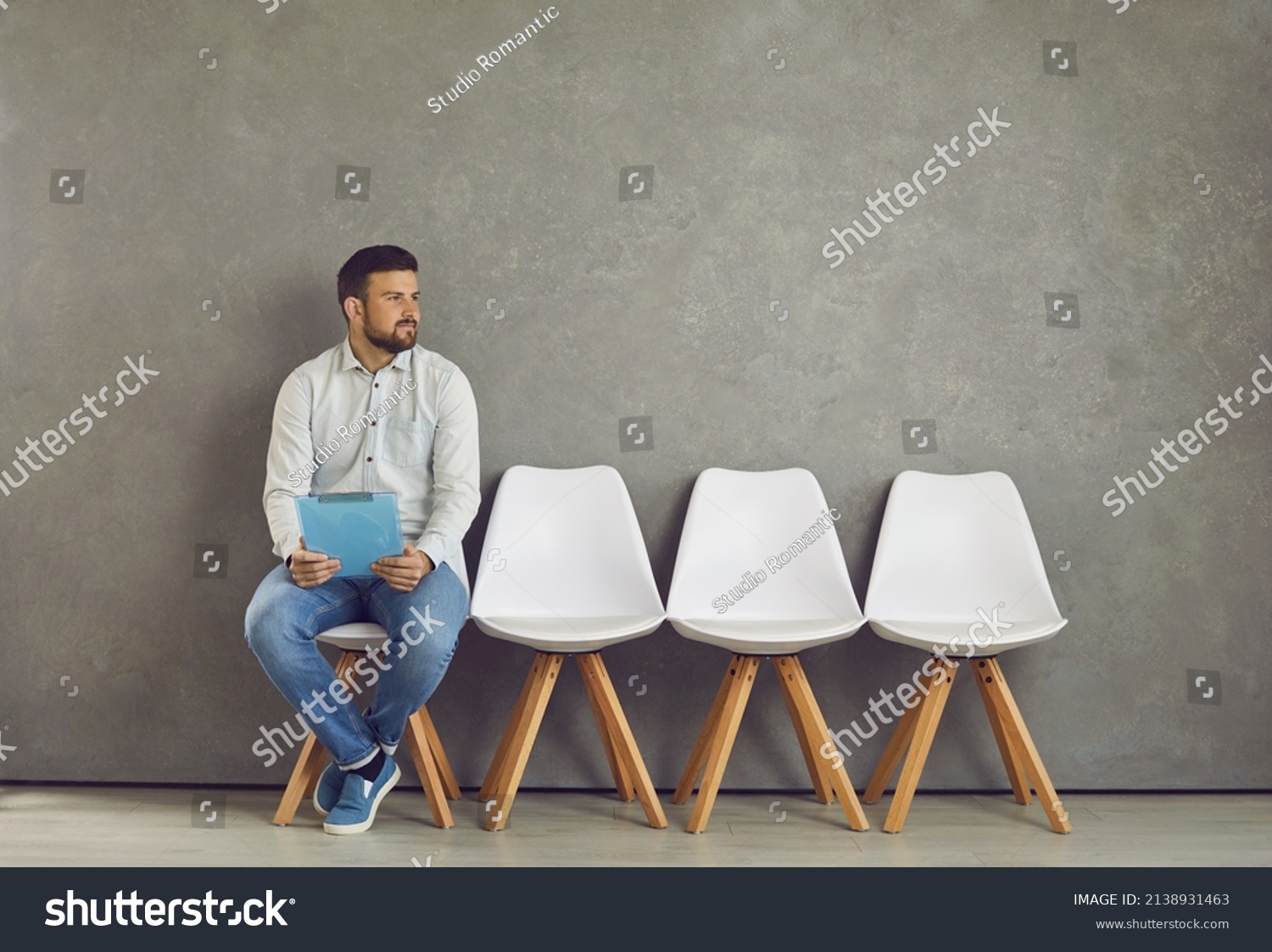 Worried young caucasian male job seeker vacancy candidate holding resume form waiting for interview meeting sitting on chair looking aside. Jobless applicant at recruitment staffing agency #2138931463